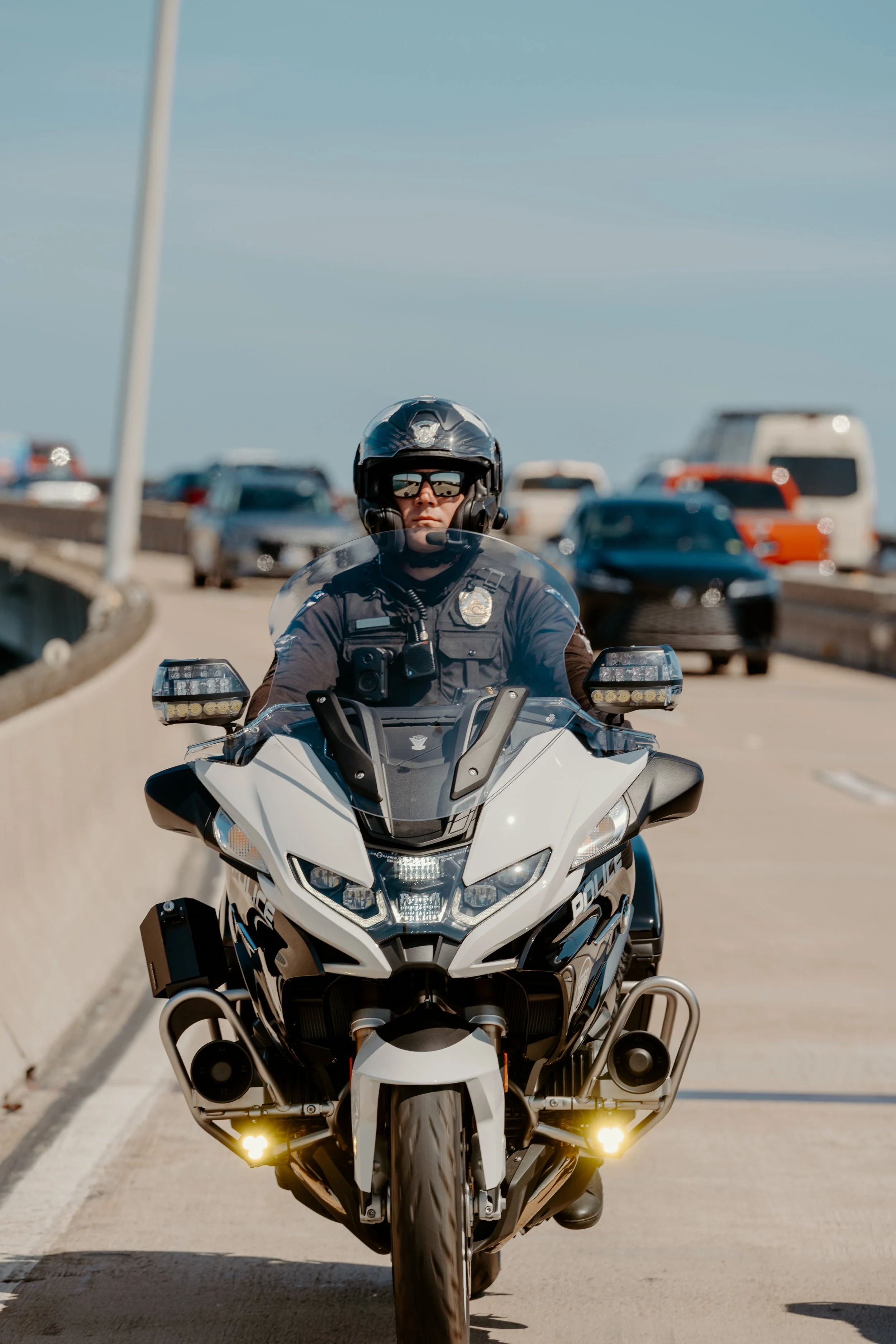 A police officer riding a motorcycle on a highway with traffic in the background.
