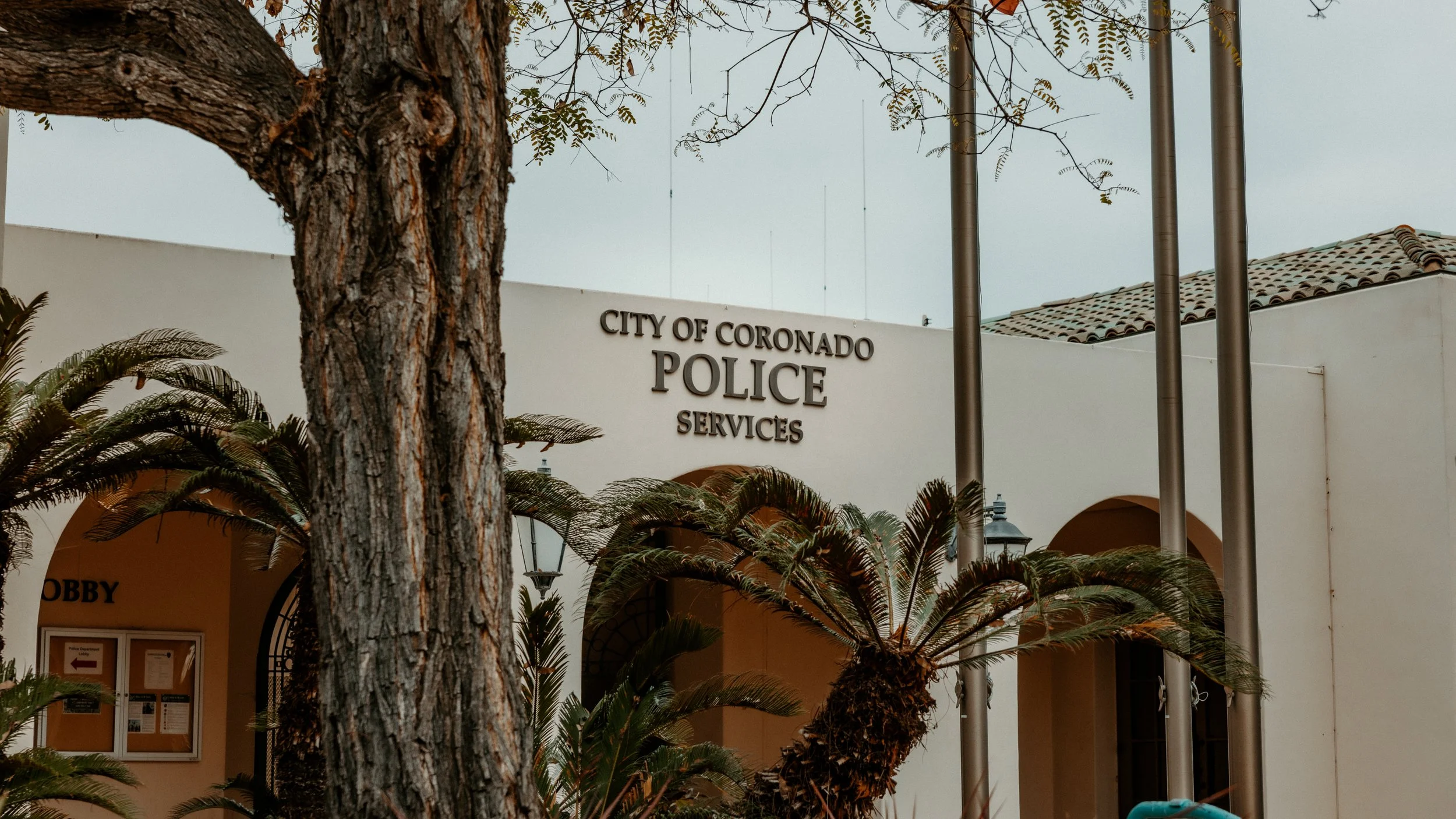 Exterior of the City of Coronado Police Services building with trees and plants in the foreground.