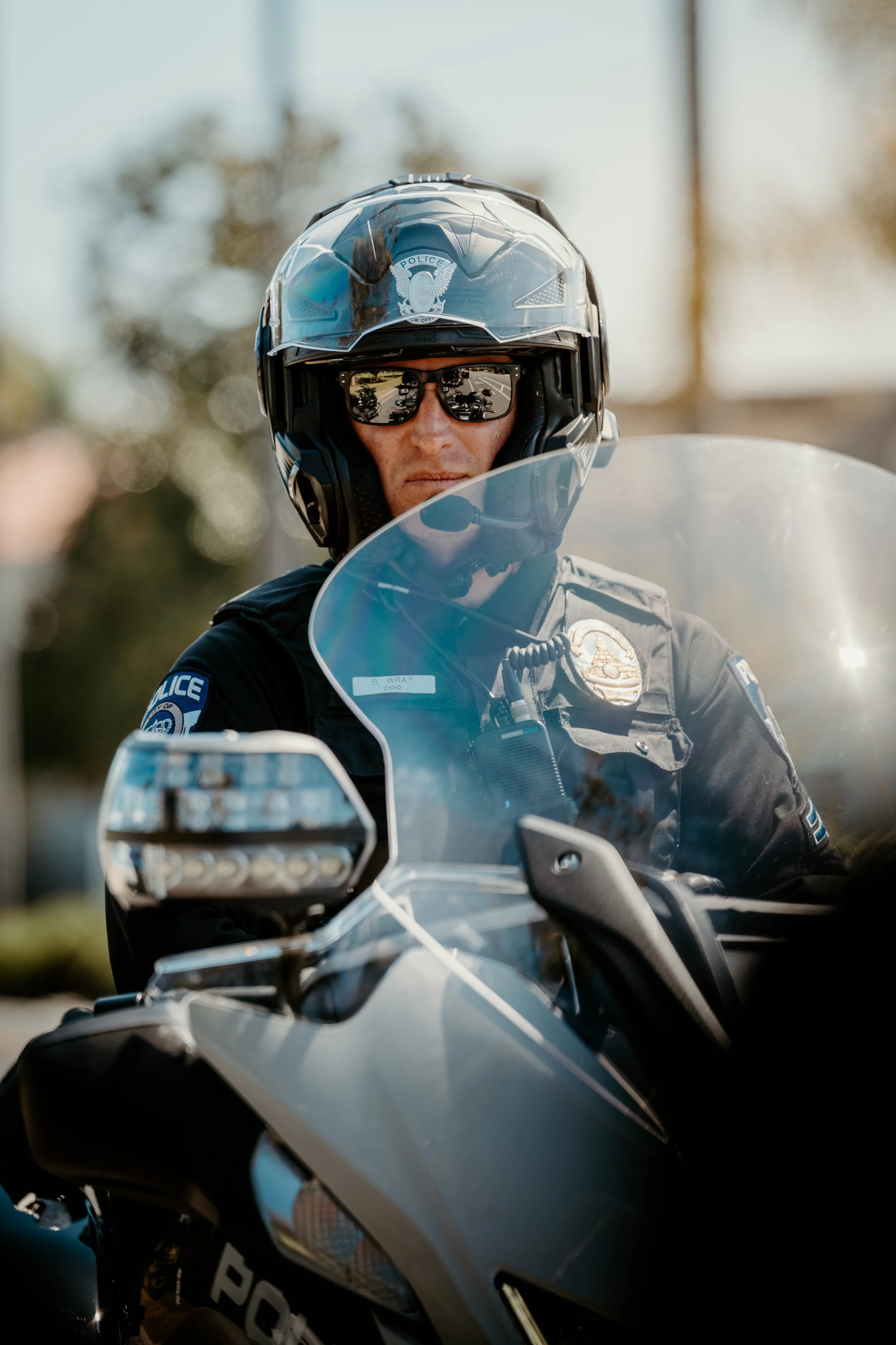 Close-up of a police officer wearing a helmet and sunglasses, sitting on a motorcycle.