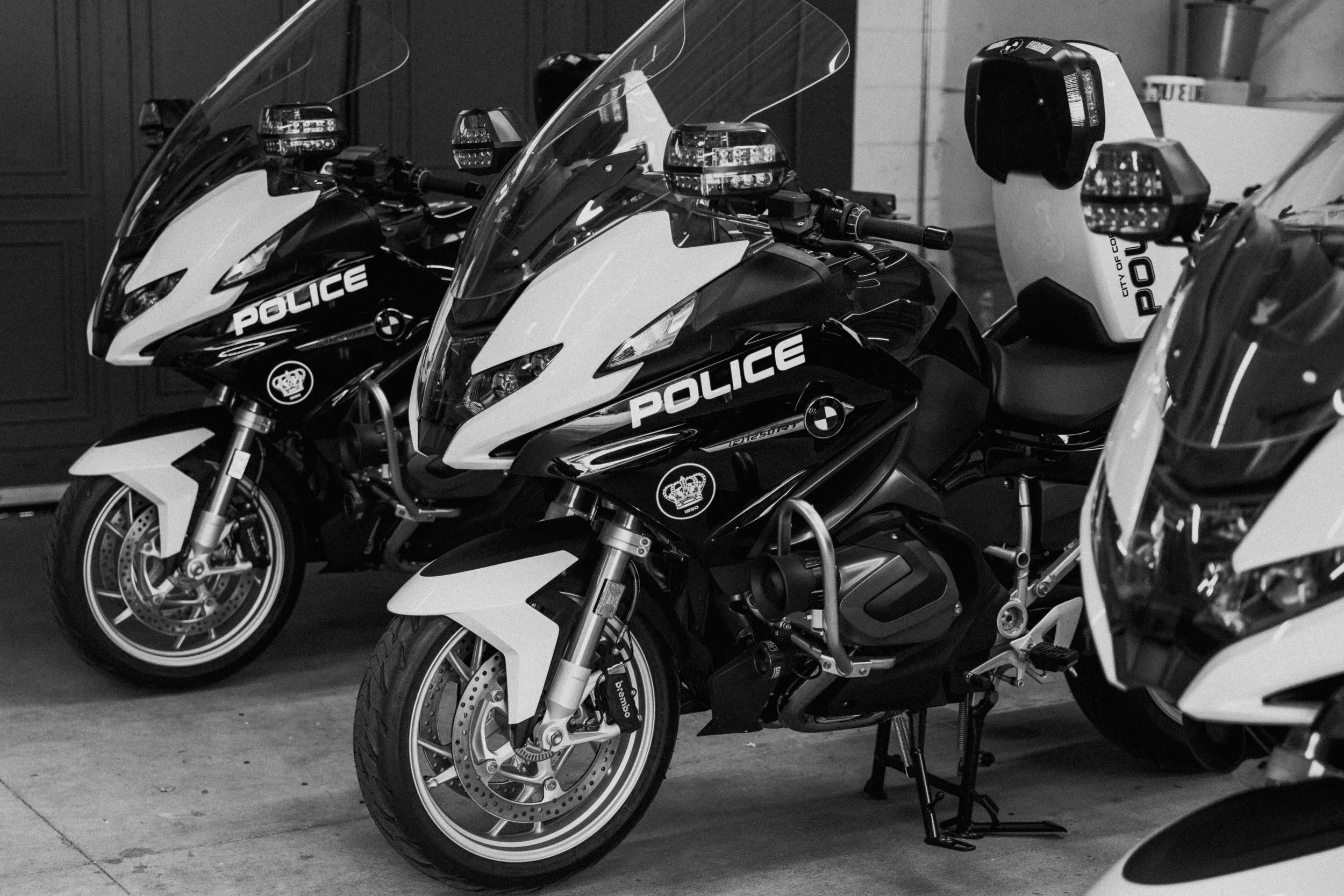 Three police motorcycles parked indoors, black and white photo.