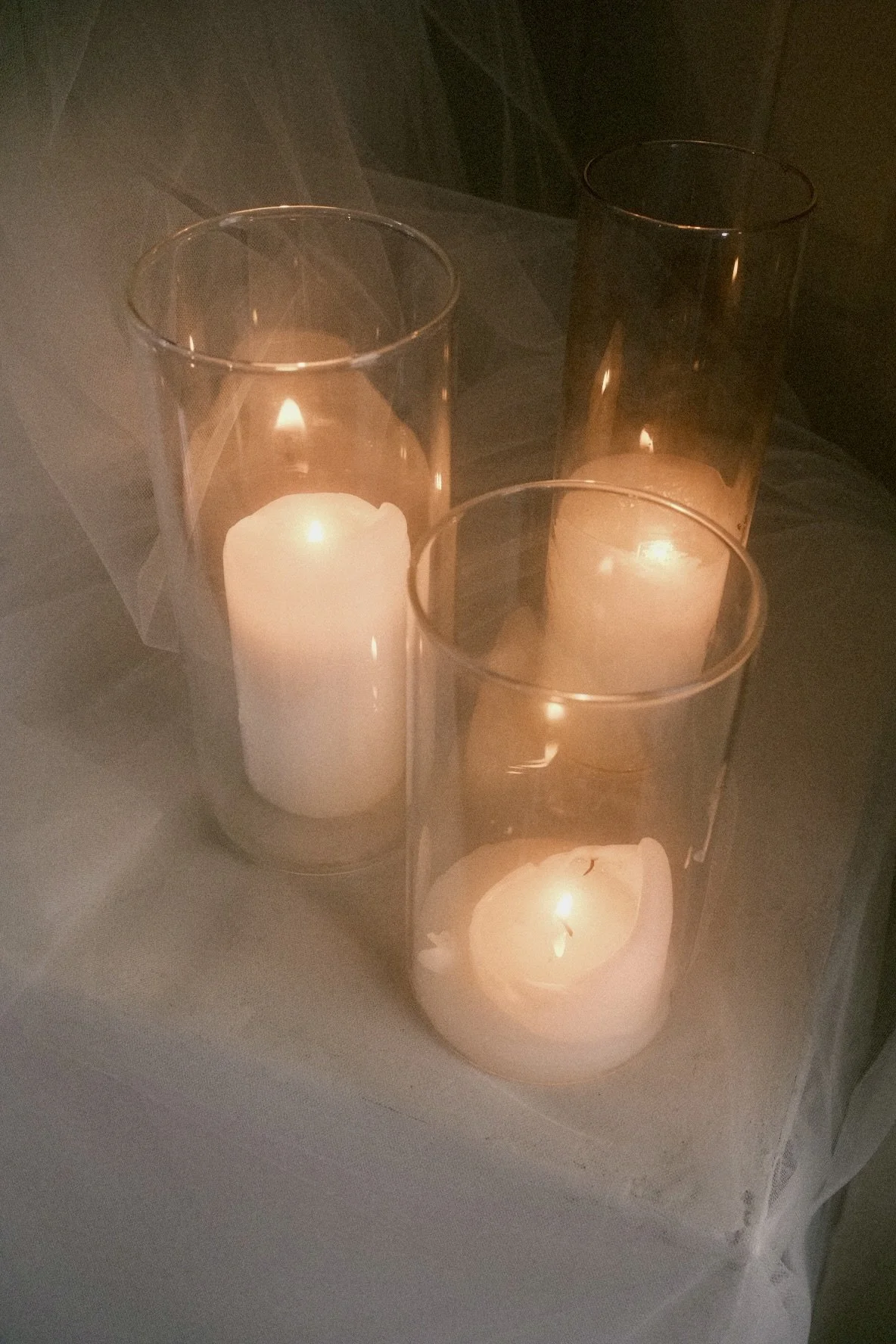 Three lit candles inside transparent glass holders on a table, creating a warm, cozy atmosphere.