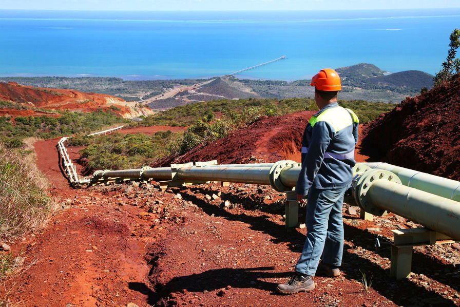 New Caledonian worker wearing an orange safety helmet and a reflective jacket inspecting a pipeline on a mountain.