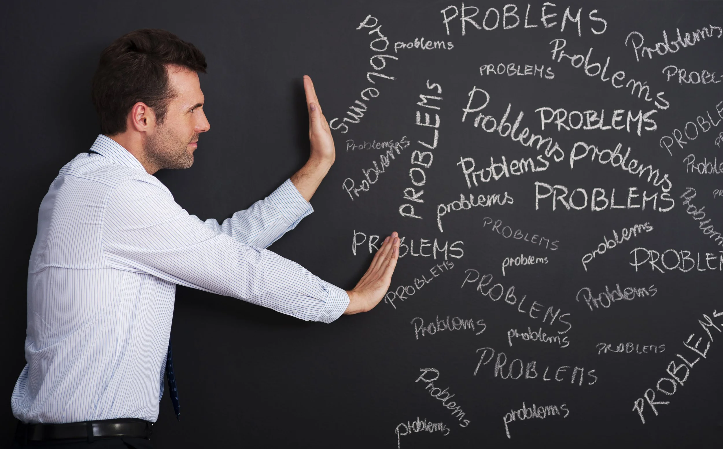 Problem Conflict Resolution represented by a business man standing in front of a blackboard that has the word "PROBLEMS" written repeatedly in various sizes and orientations, with his hands raised as if trying to block or stop the words.