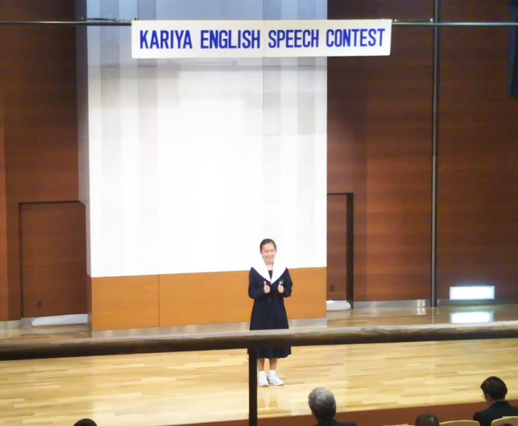 英語スピーチコンテストのステージに立つ女性と観客の風景。