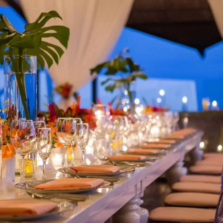 Elegant outdoor dining table set for a dinner with glassware, plates, napkins, candles, and floral centerpieces at dusk.