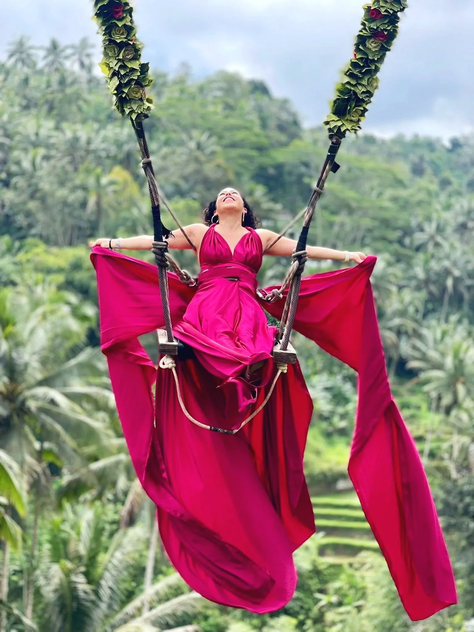 Woman in a pink dress swinging on a jungle swing in Bali.