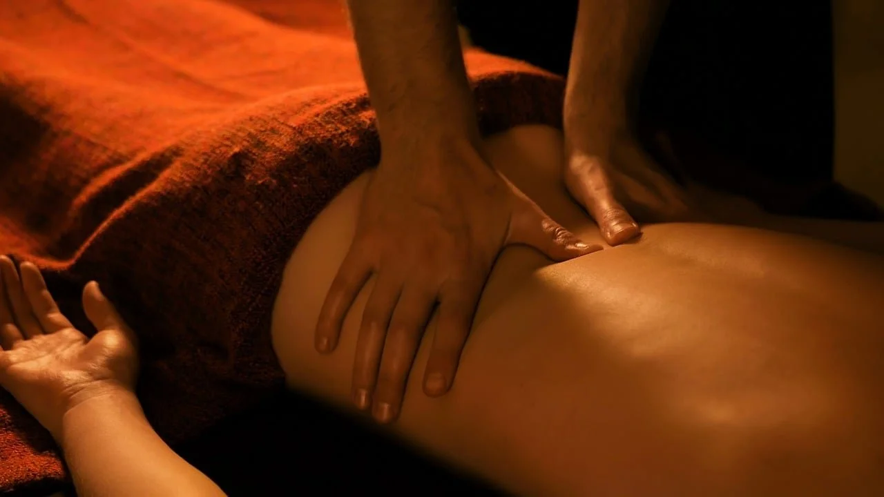 Close-up of a massage session with a person receiving a massage and another person giving the massage, focusing on their hands and back.