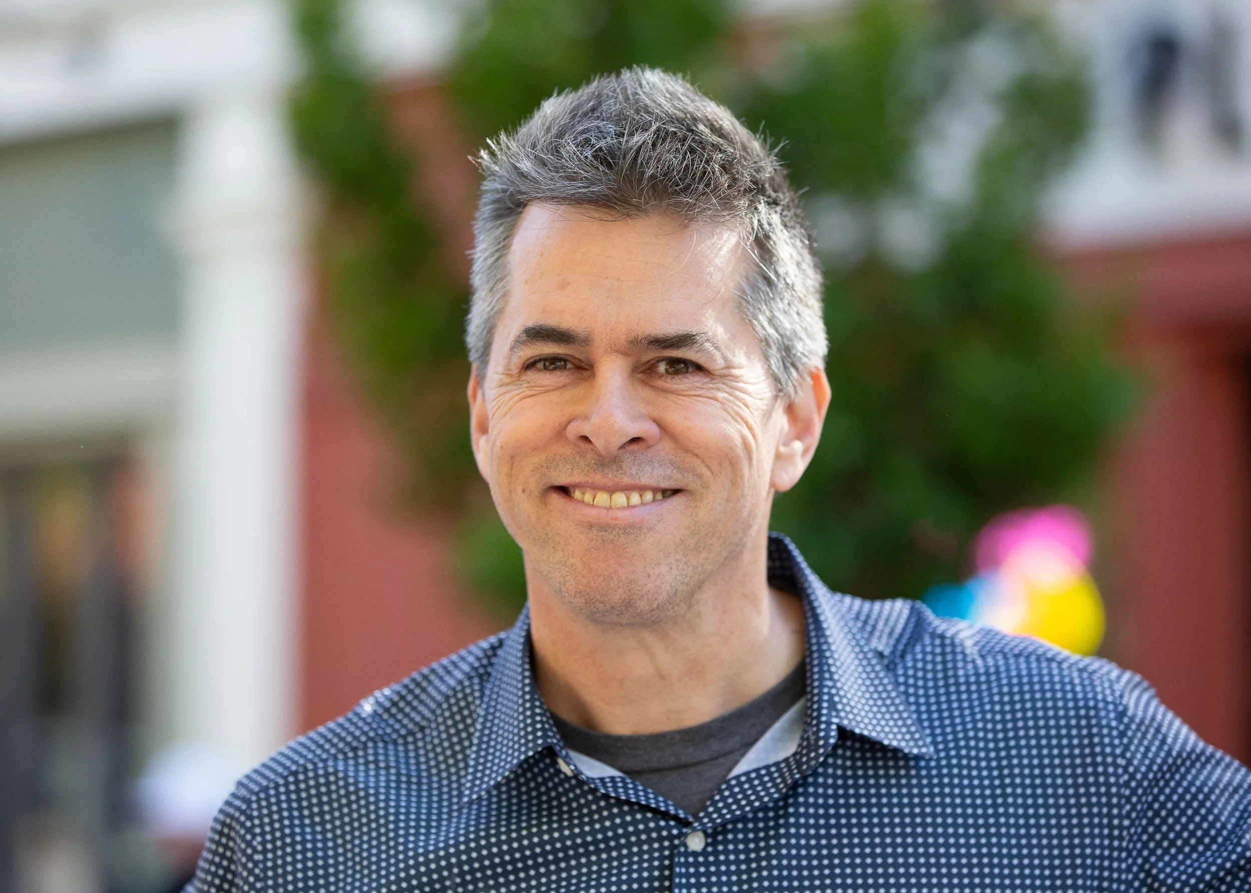 Chip outside, wearing a blue and white polka dot shirt, with a blurred background including colorful balloons and trees.