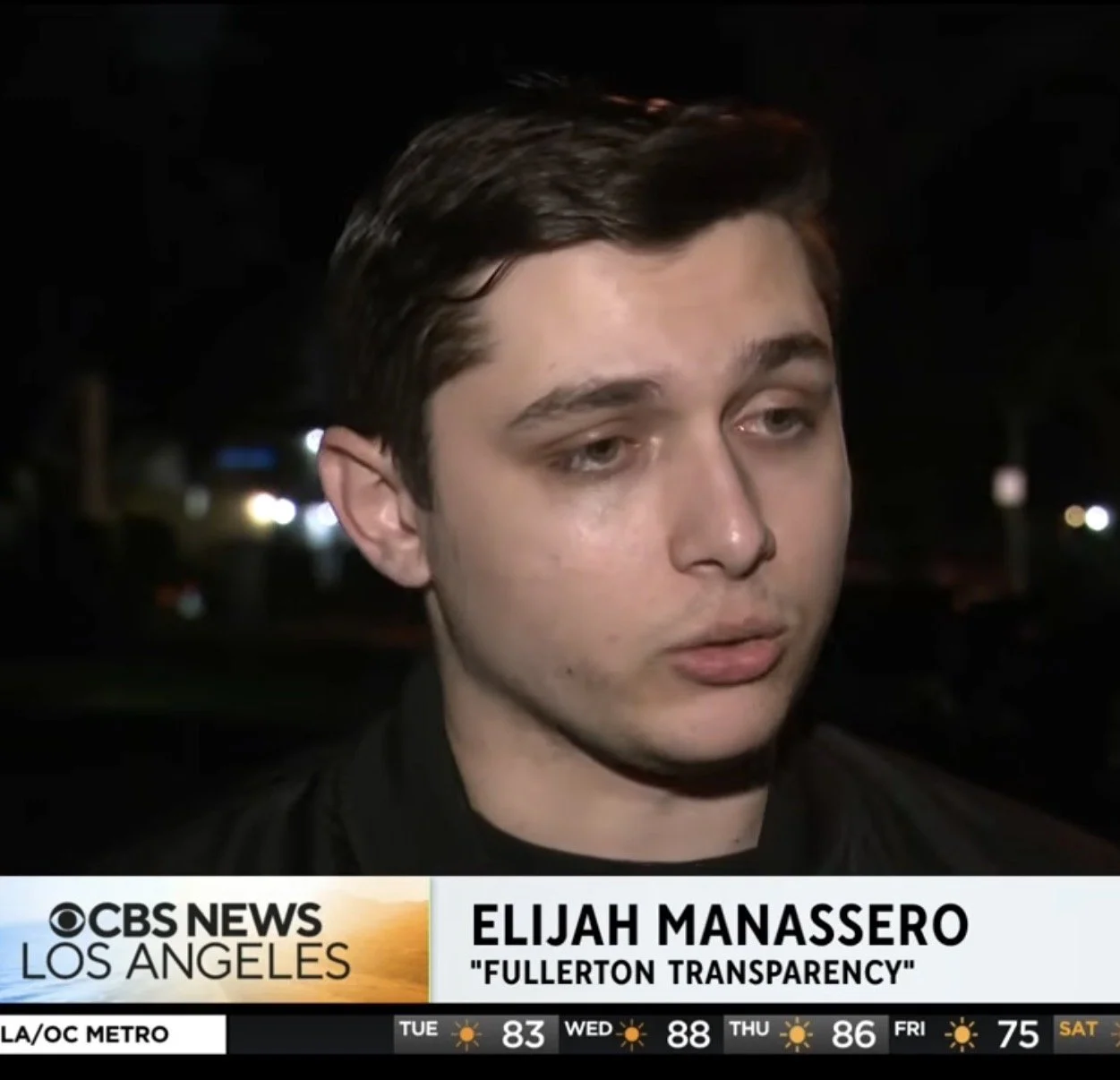 Close-up of a young man with dark hair and light skin being interviewed at night on CBS News Los Angeles, with a caption attributing him as Elijah Manassero from 'Fullerton Transparency'.