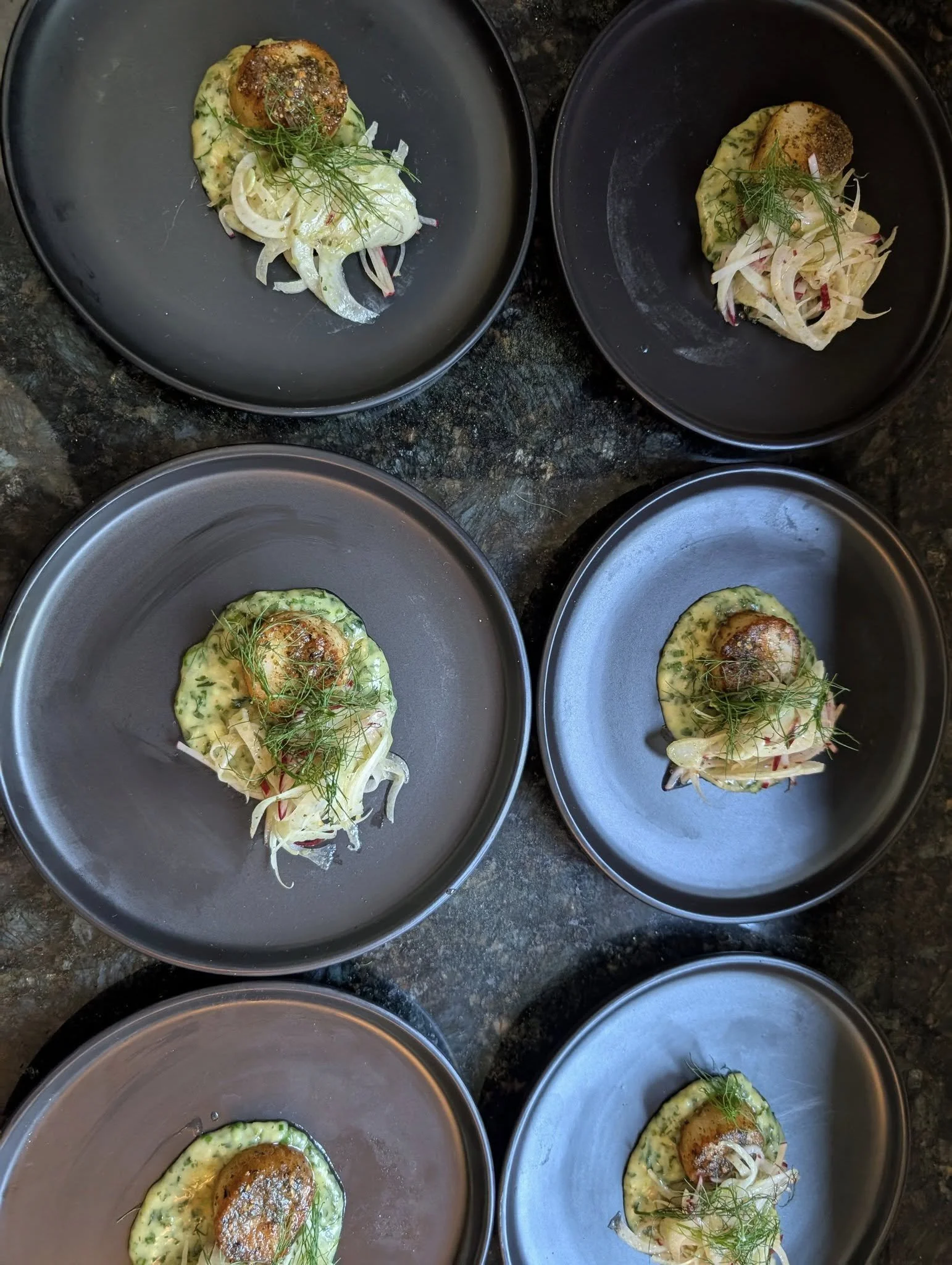 Six black plates with stuffed food topped with herbs, served on a dark surface.
