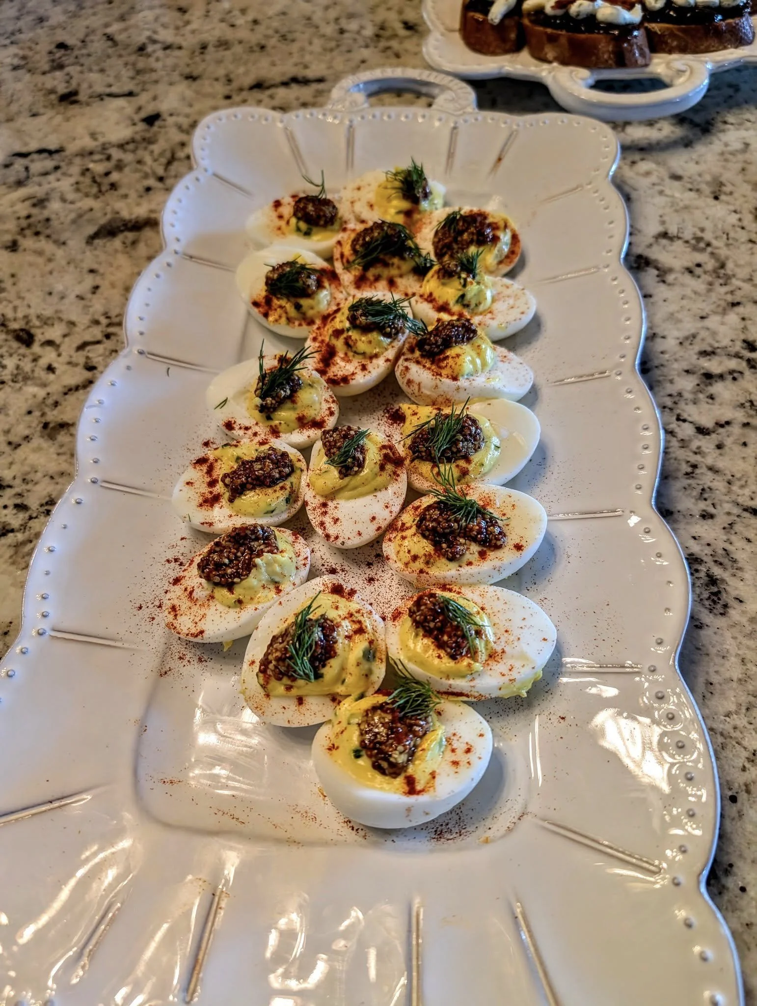 Deviled eggs topped with herbs and spices on a decorative white platter.