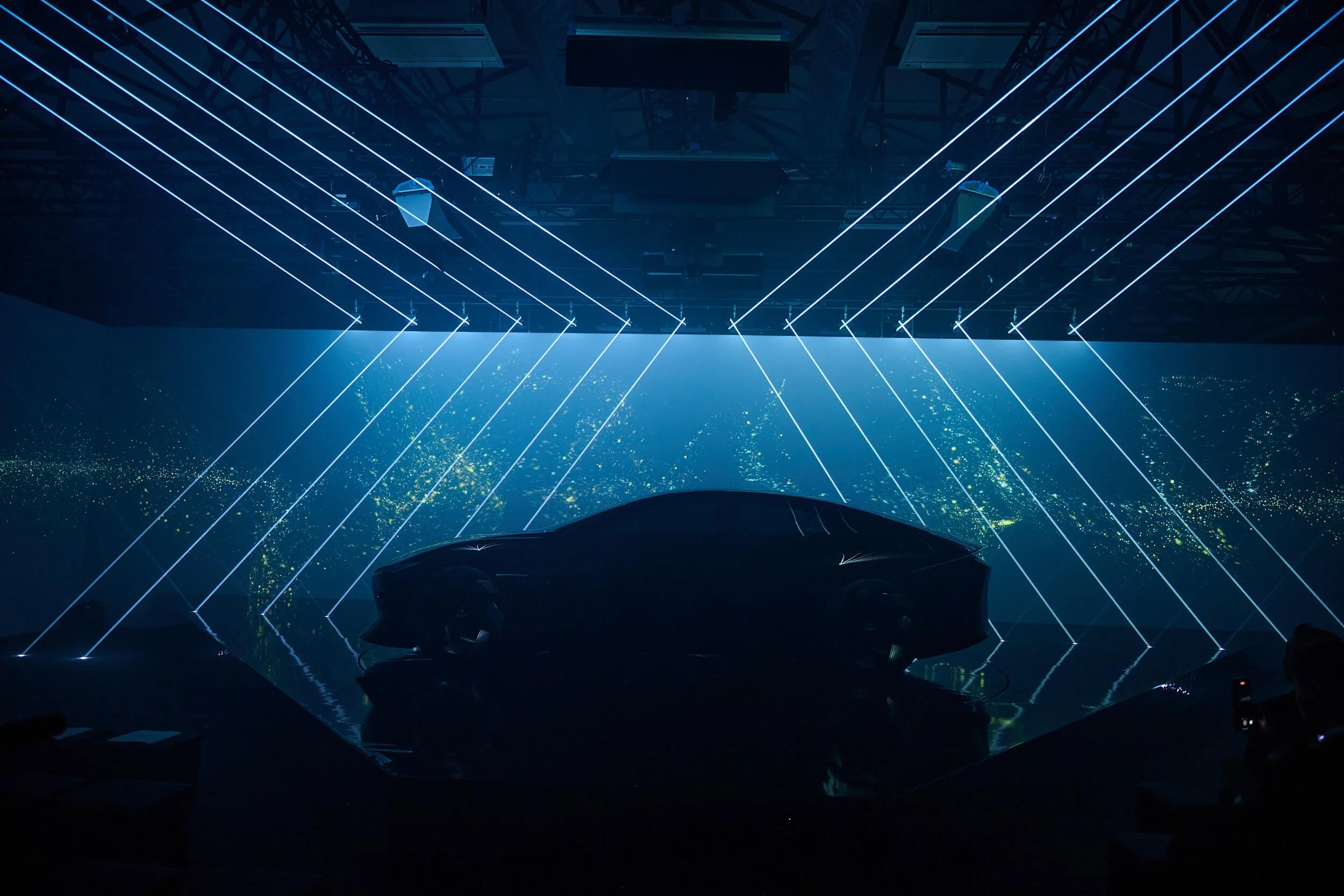 Stage with blue laser lights, large screen, and audience below.