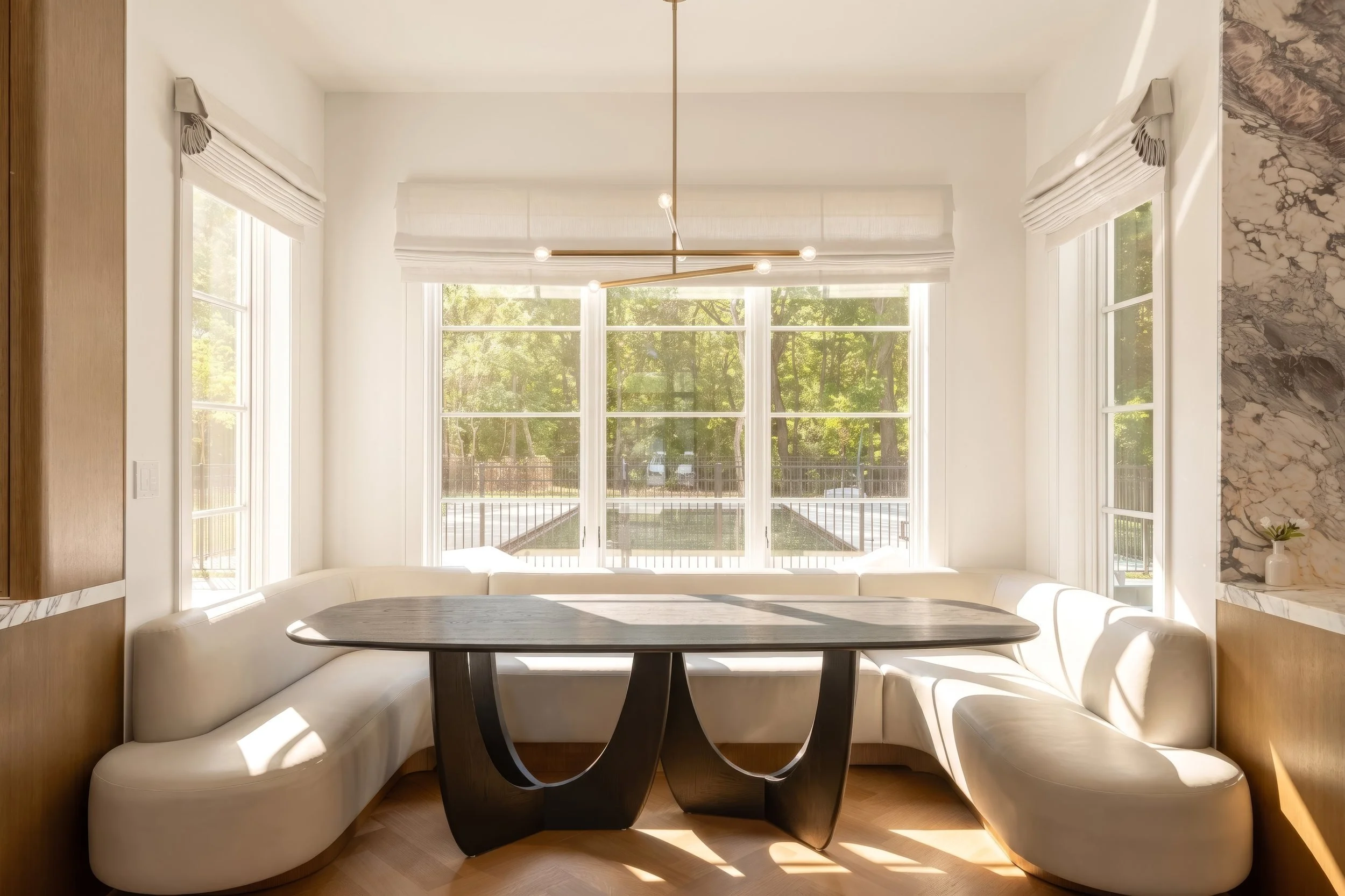 Curved upholstered breakfast nook with a sculptural table and garden windows