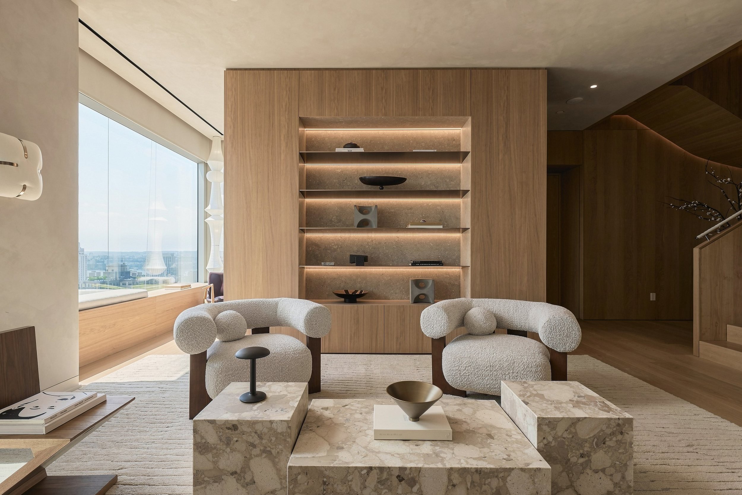 Lounge with boucle chairs, stone coffee table and lit oak shelving