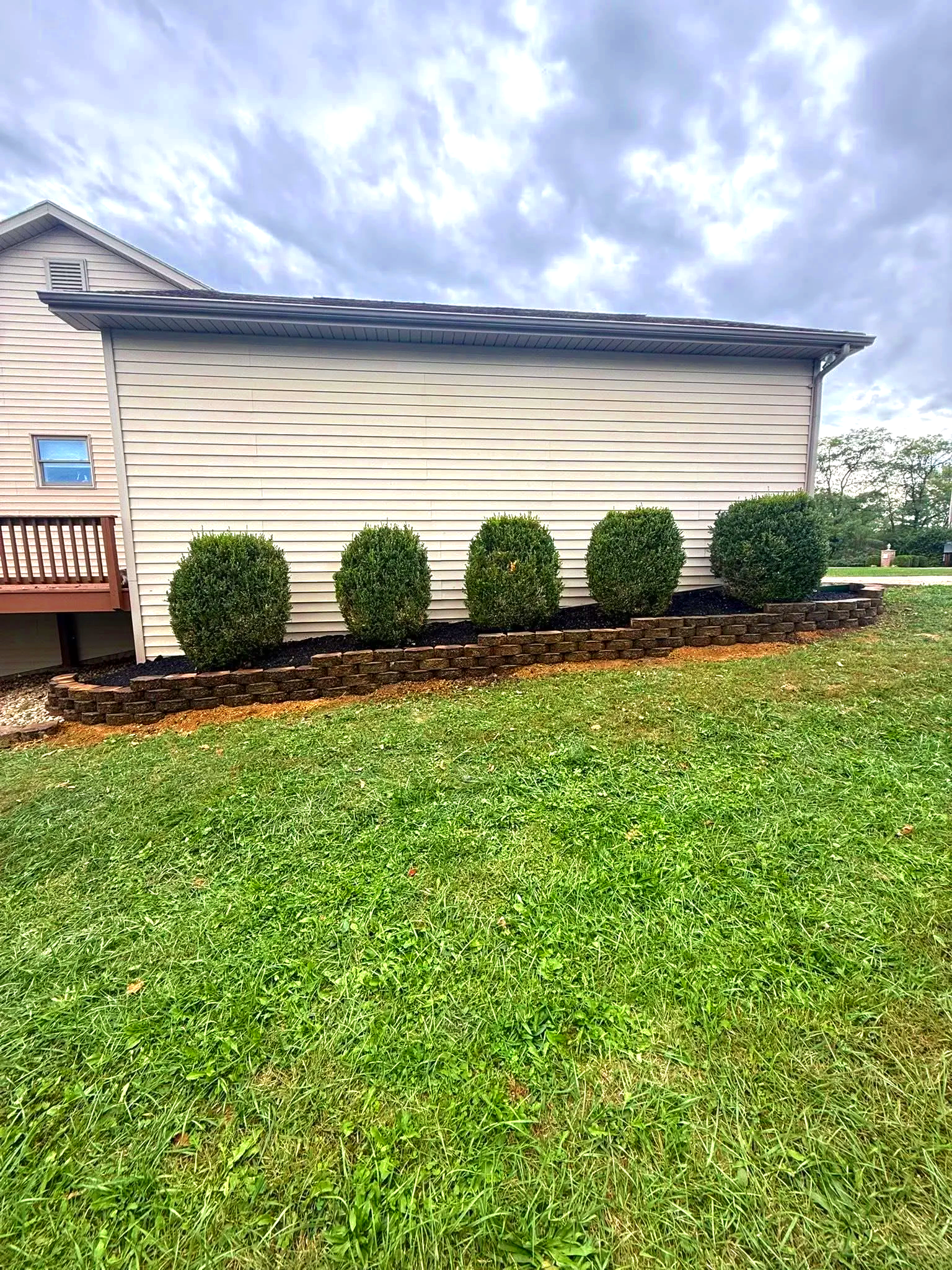 A landscaped raised flower bed with dark mulch and a freshly built retaining wall, under a cloudy sky.