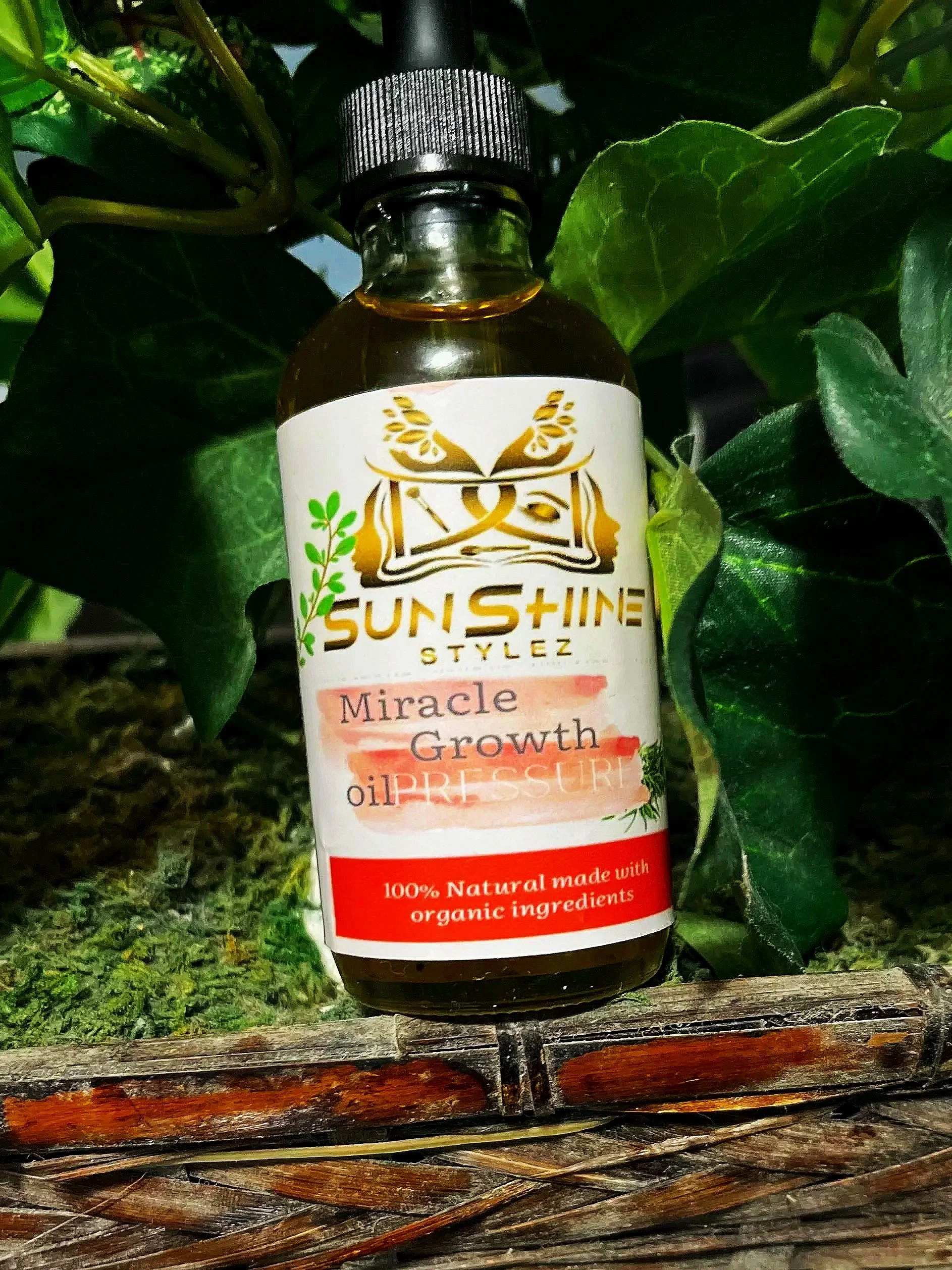 A small bottle of Sun Shine Stylez Miracle Growth Oil hanging on green ivy leaves with a natural woven surface beneath.