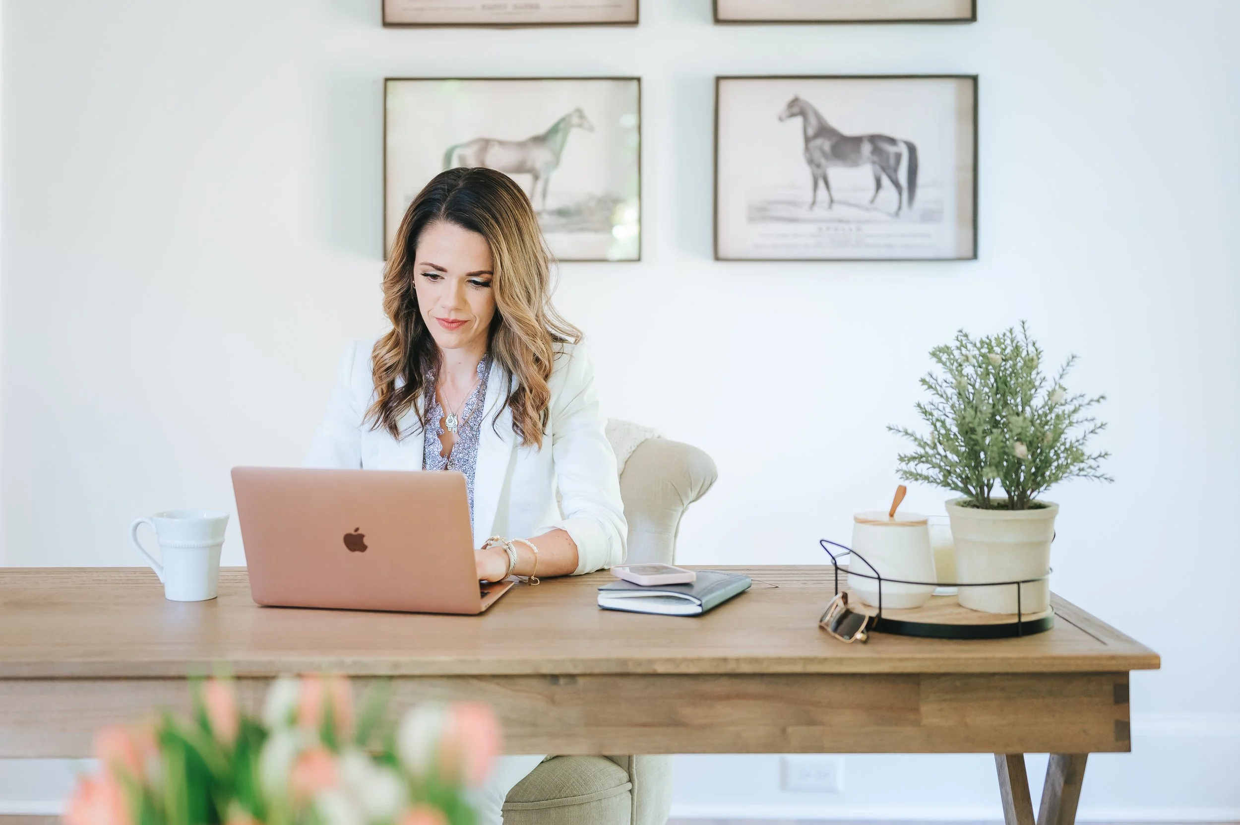 female real estate agent in white jacket sitting at desk in office and typing on laptop