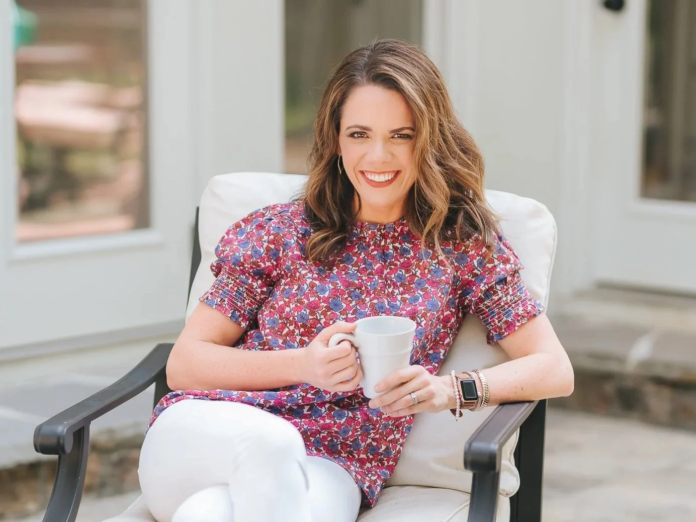female social media manager in pink shirt sitting on a patio drinking coffee from a white mug