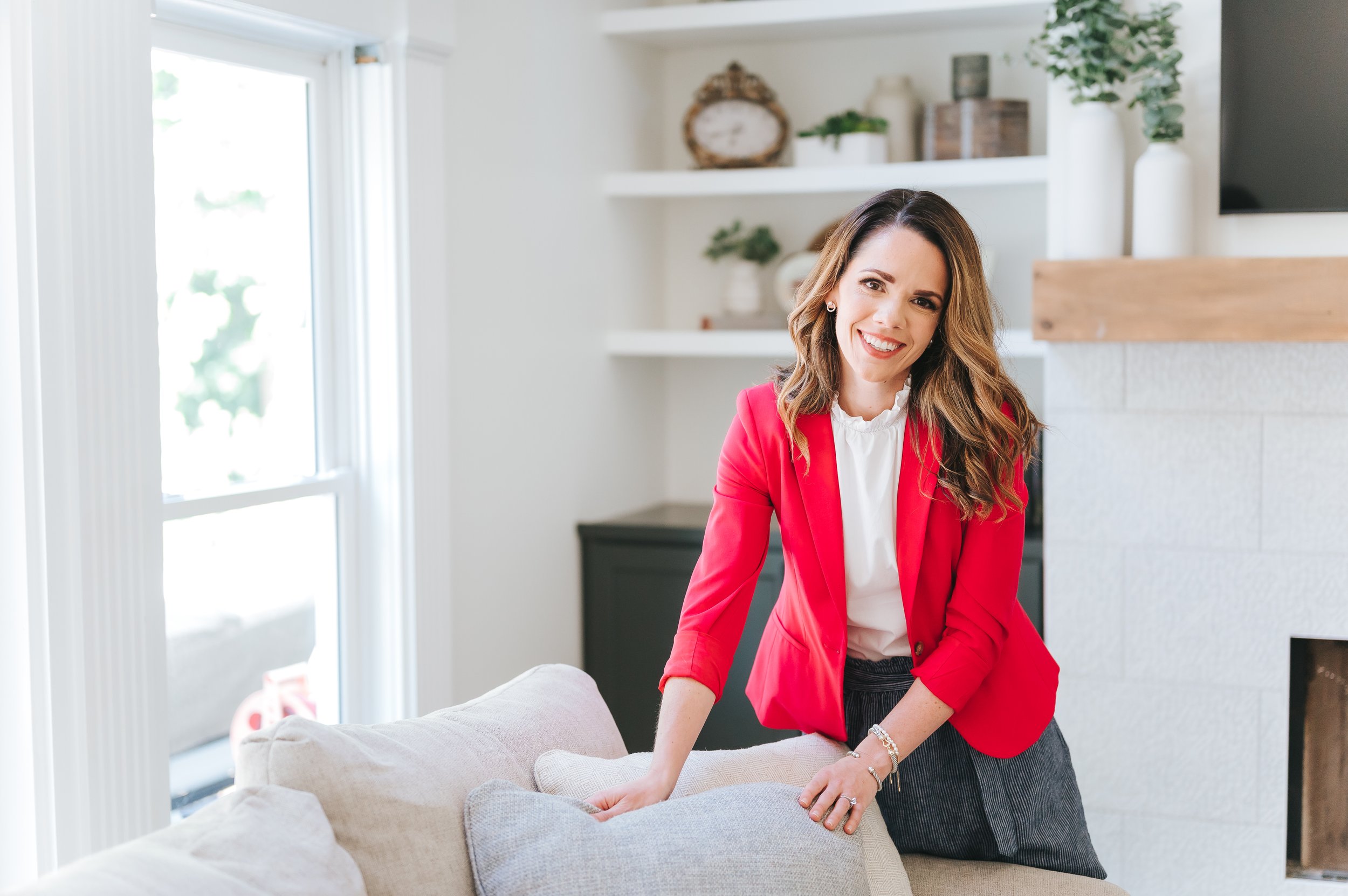 female real estate agent in a bright pink jacket staging a couch in a luxury home
