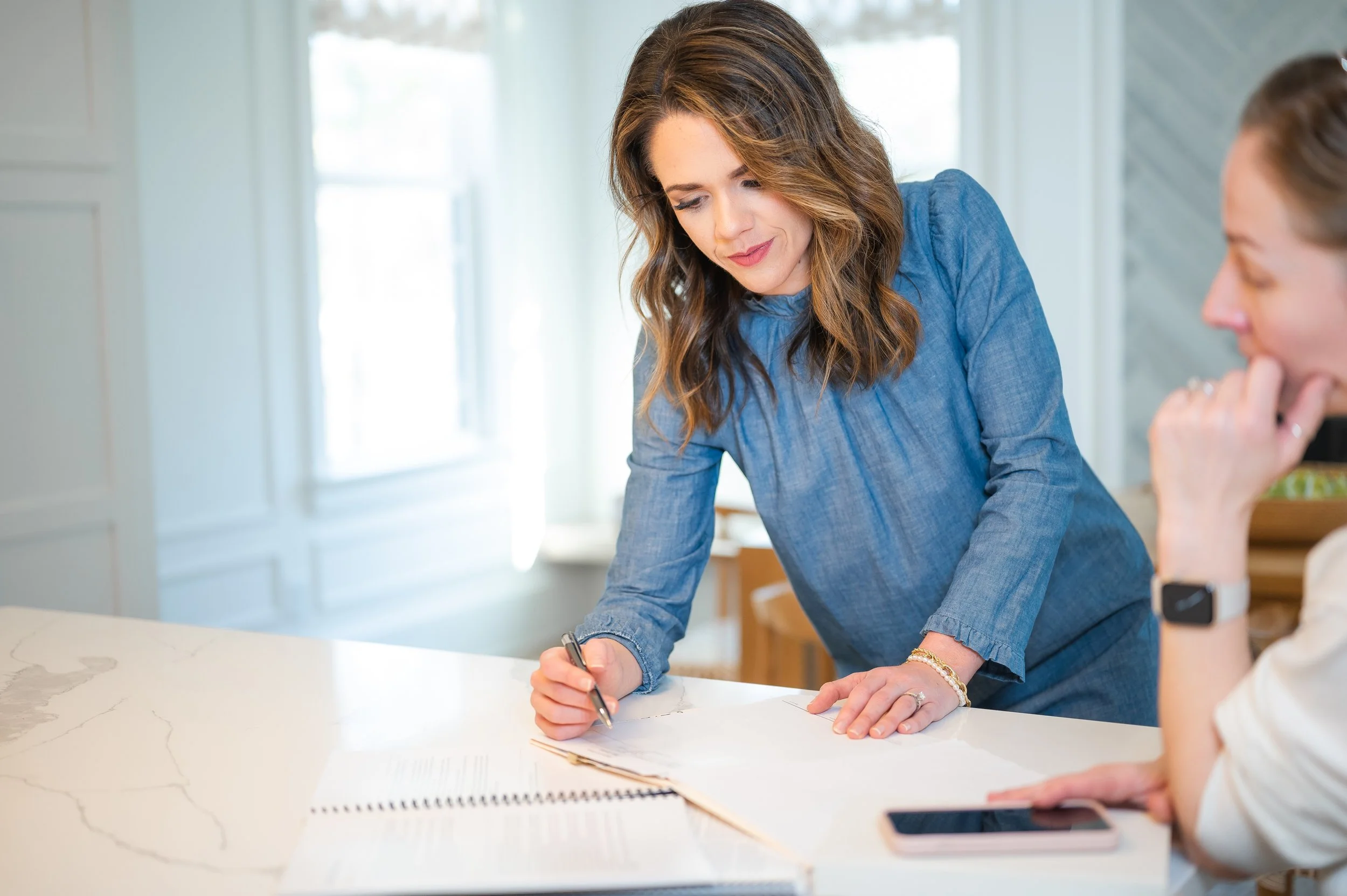 female real estate agent in denim dress reviewing a contract with a female client in a kitchen