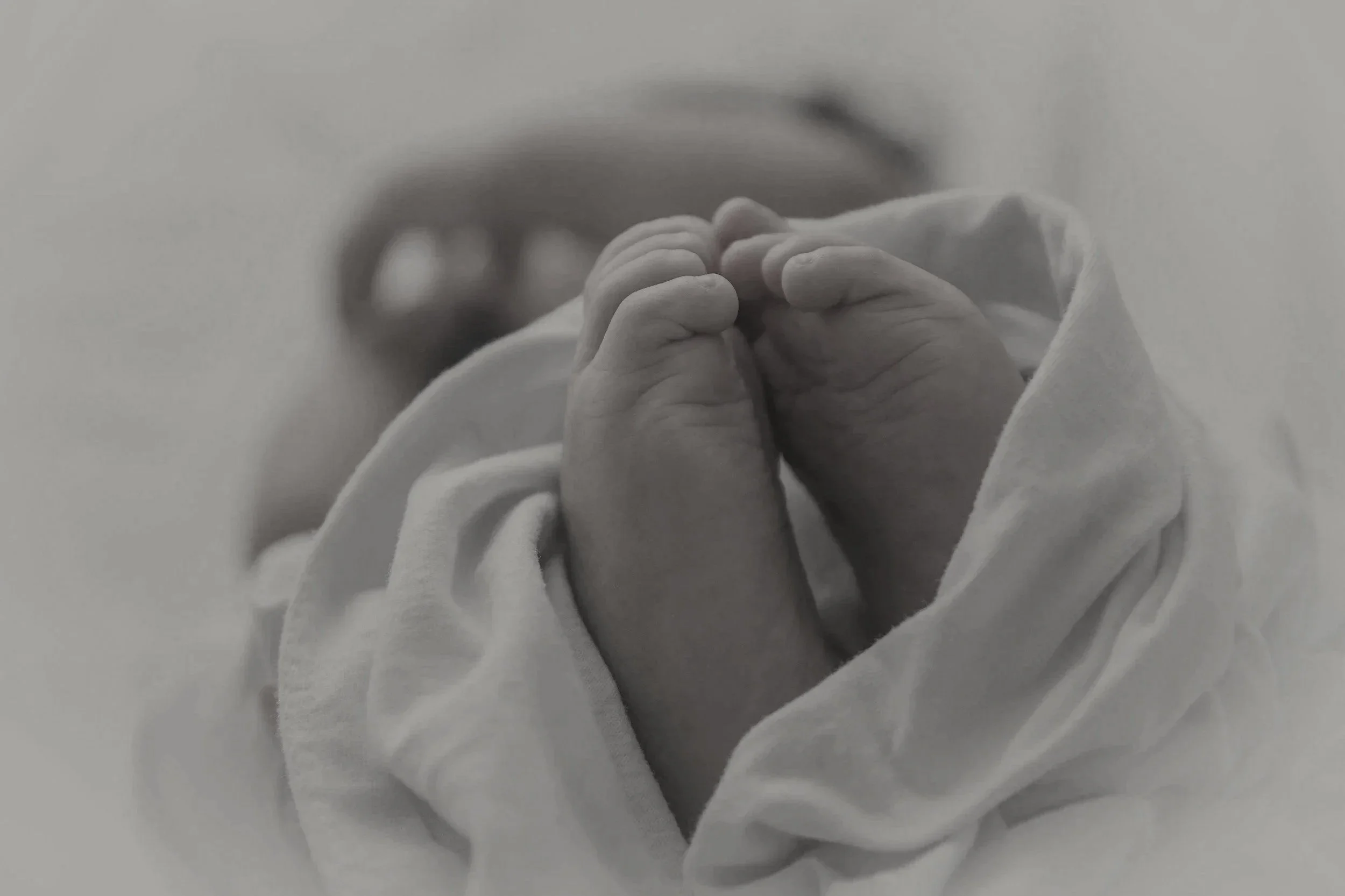 Close-up of a newborn baby's tiny hands clasped together, wrapped in a soft blanket.