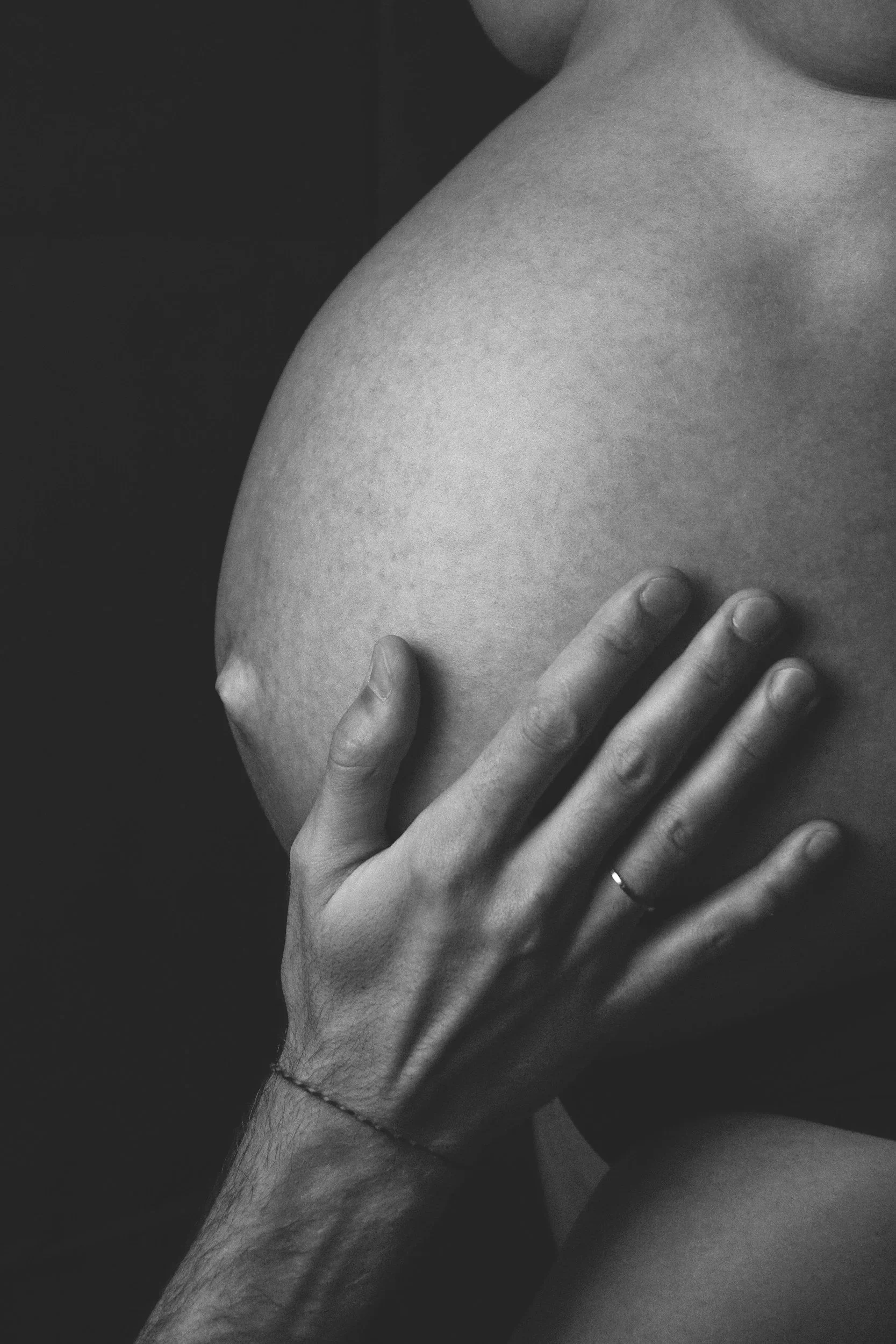 Close-up of a person's hand gently resting on a pregnant belly in black and white