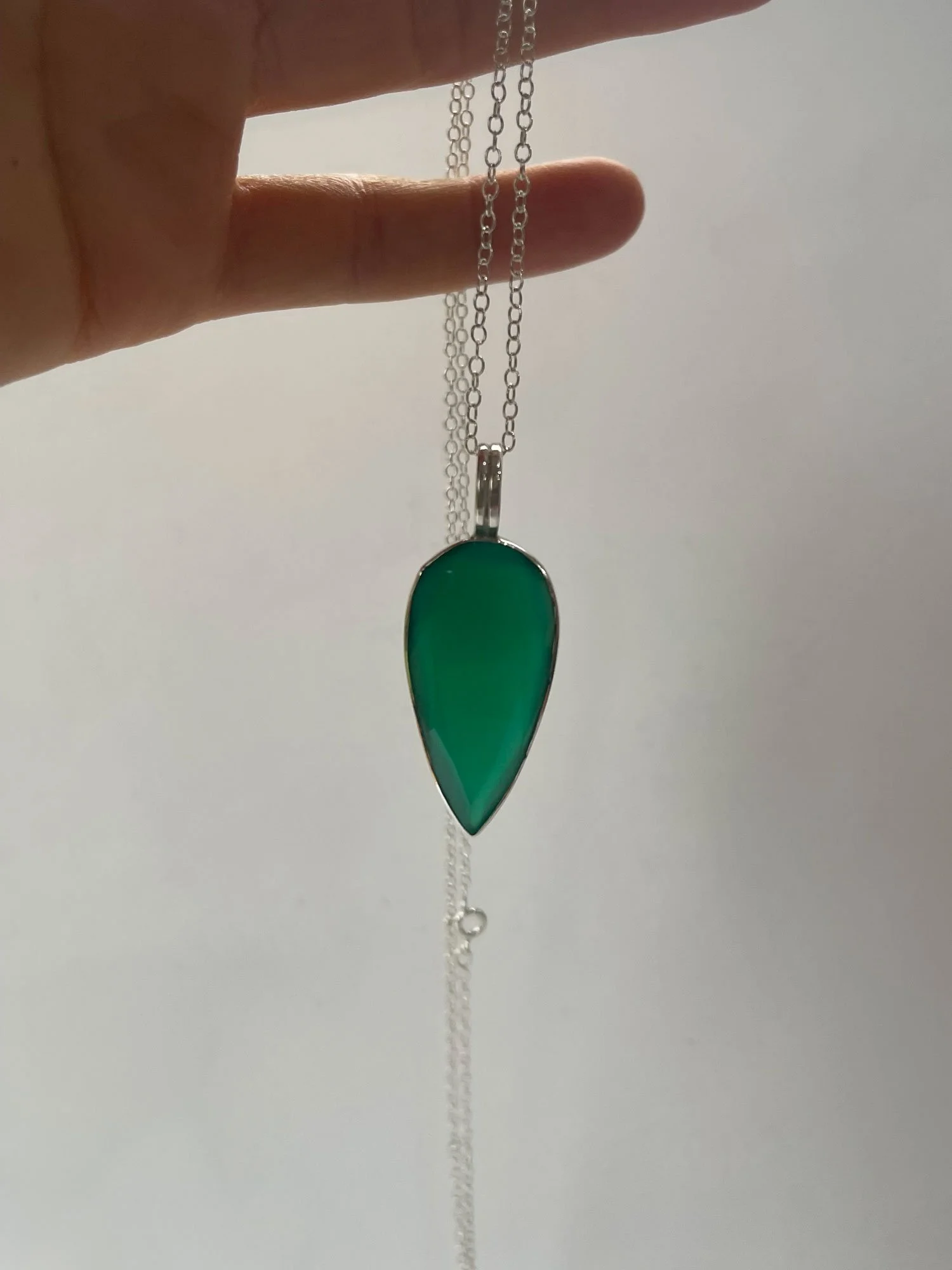 teardrop green onyx pendant hanging from finger