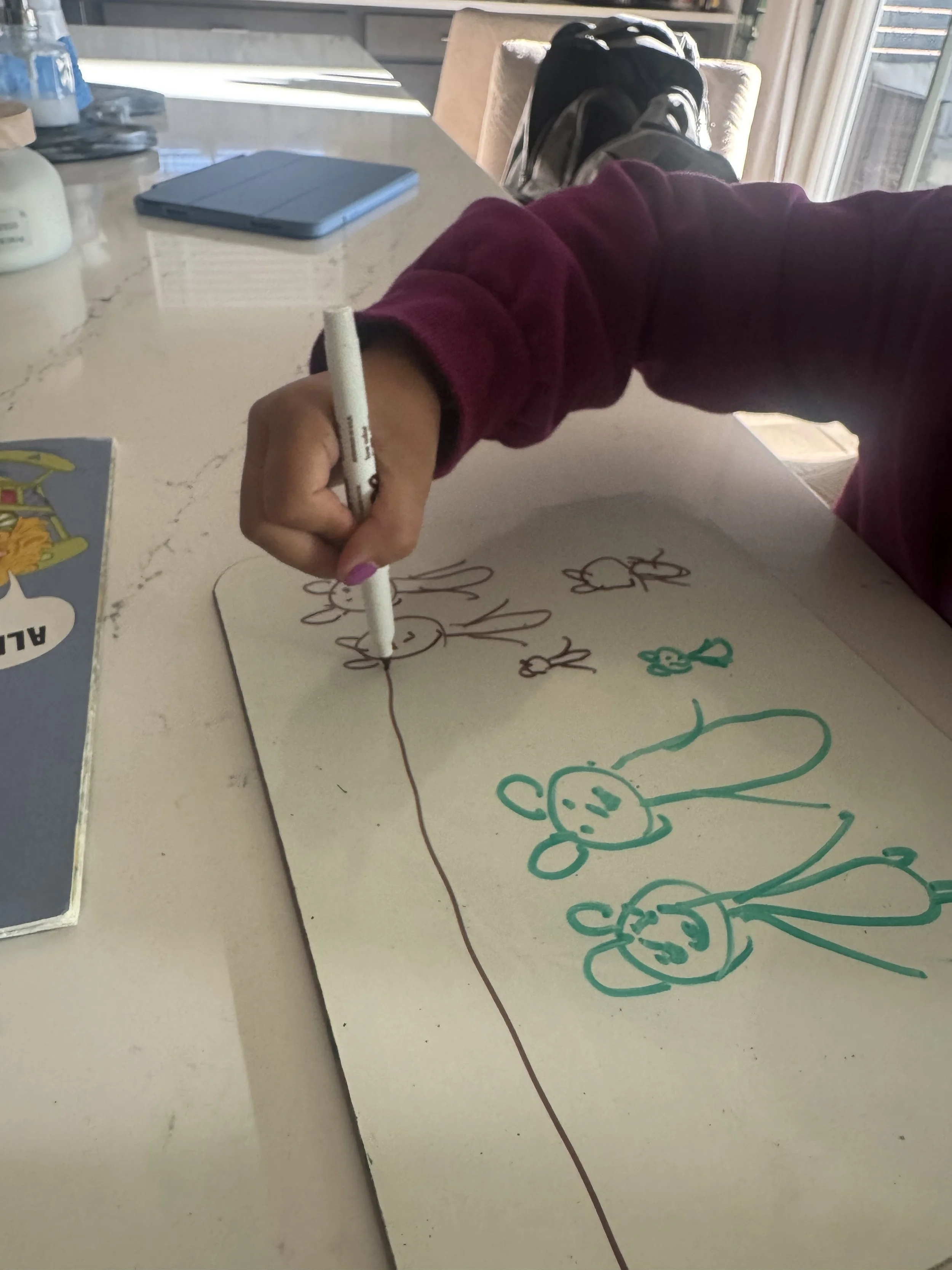 Child drawing on a sheet of paper with colorful markers, depicting animals and characters resembling bunnies and mice.