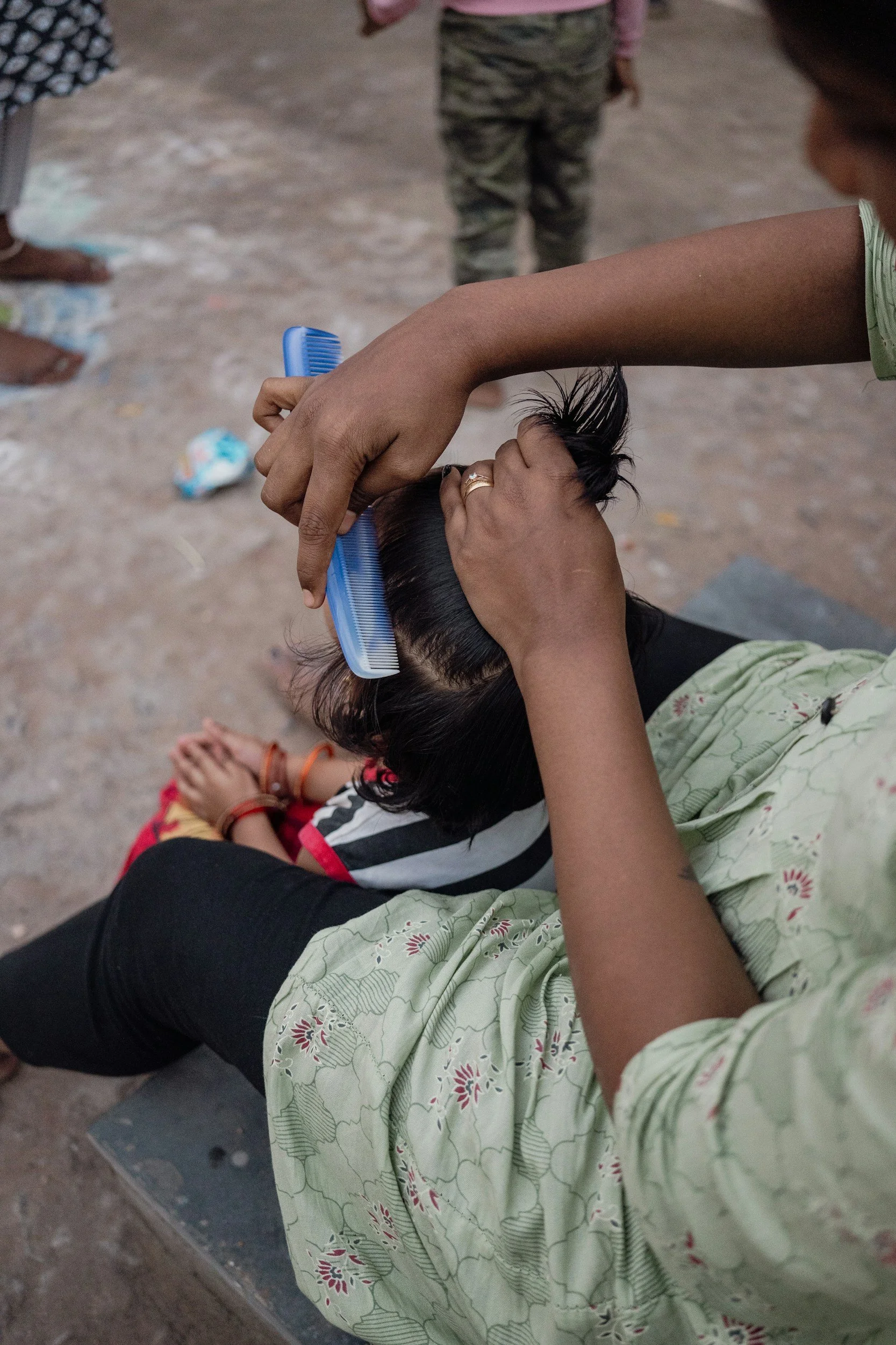 A woman is cutting a child's hair with a blue comb outdoors.