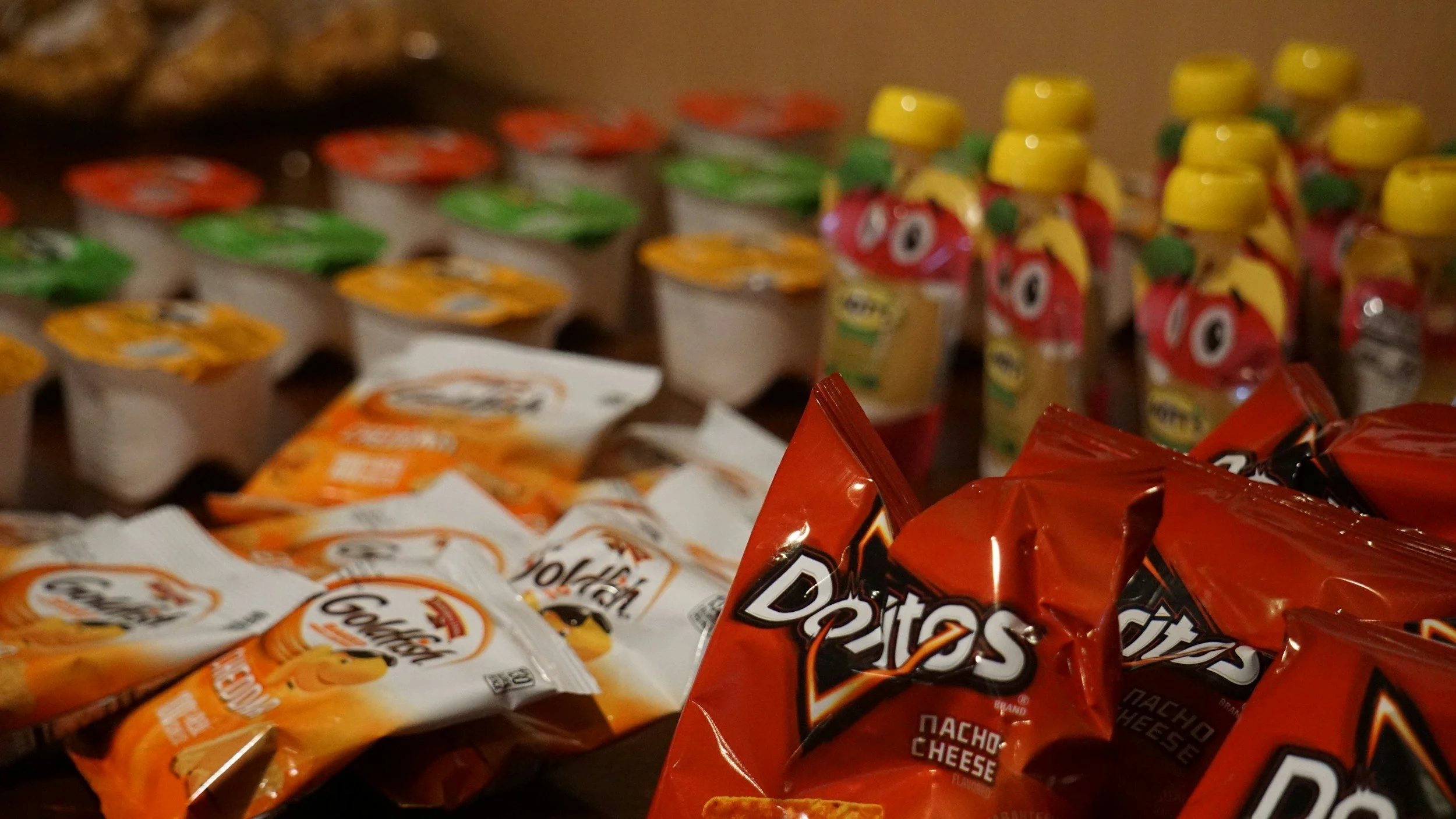 Various snack items on a table, including bags of Doritos Nacho Cheese chips, small packs of cookies, and small juice bottles with colorful labels.