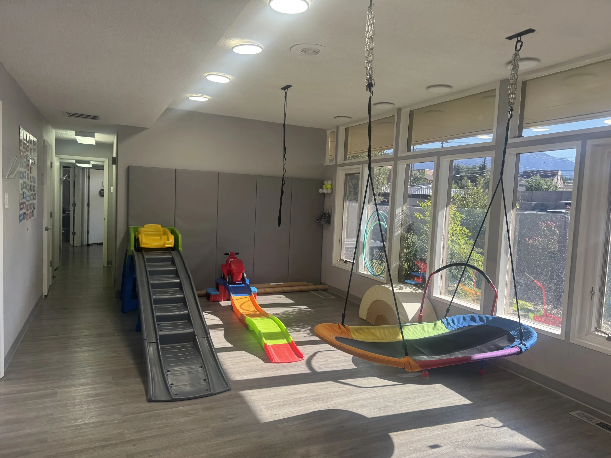 Indoor play area with a multi-colored baby swing, a small slide, a riding toy, and a rainbow-colored slide.