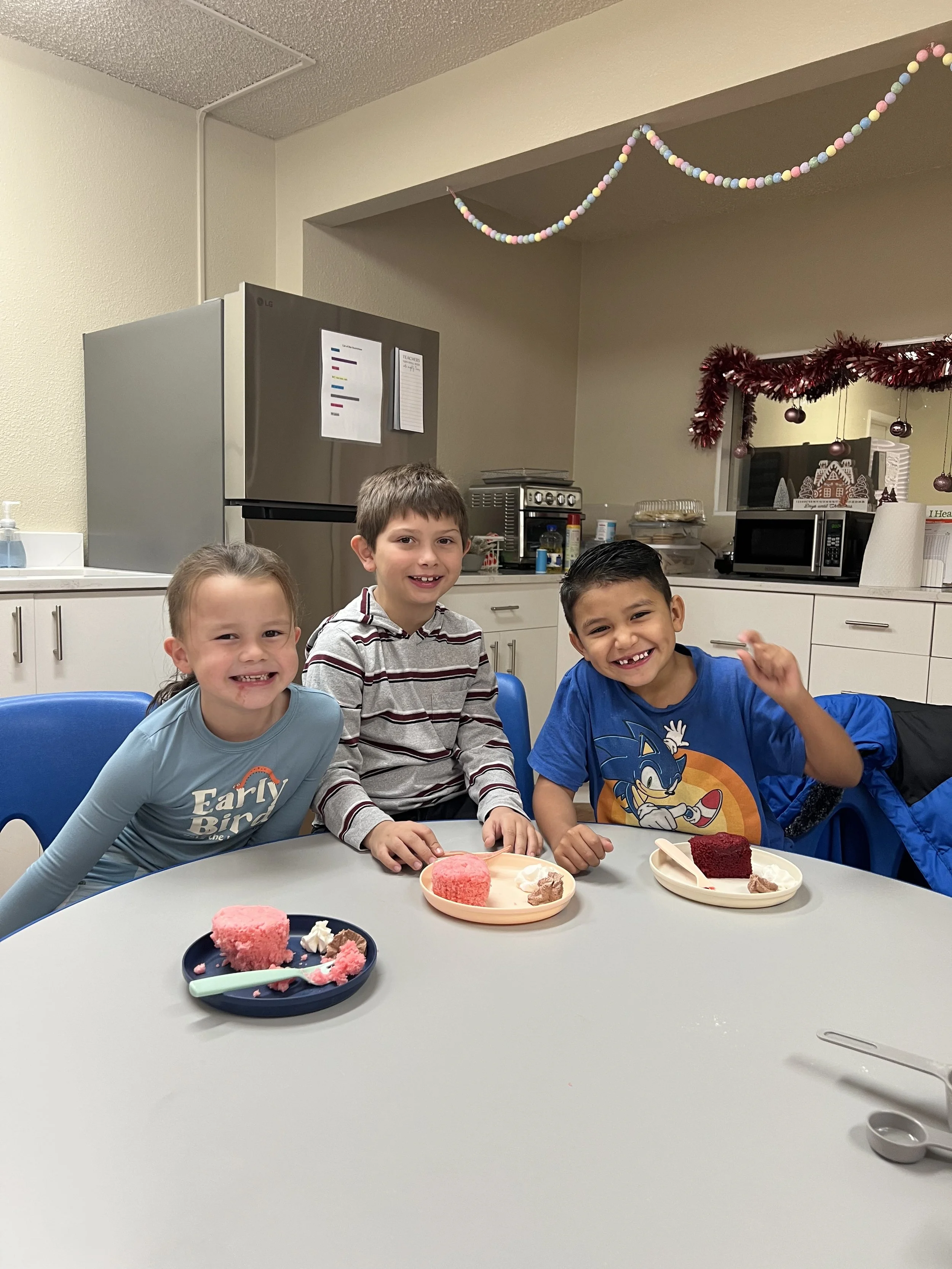 Three children sitting at a table with plates of cake and smiling.