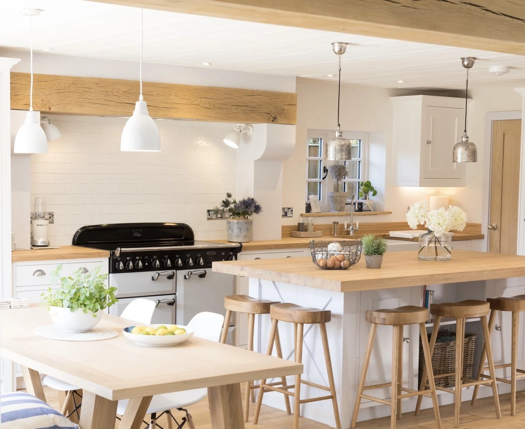 Modern kitchen with white cabinets, wooden countertops, a black stove, hanging pendant lights, and various plants and flowers for decoration.