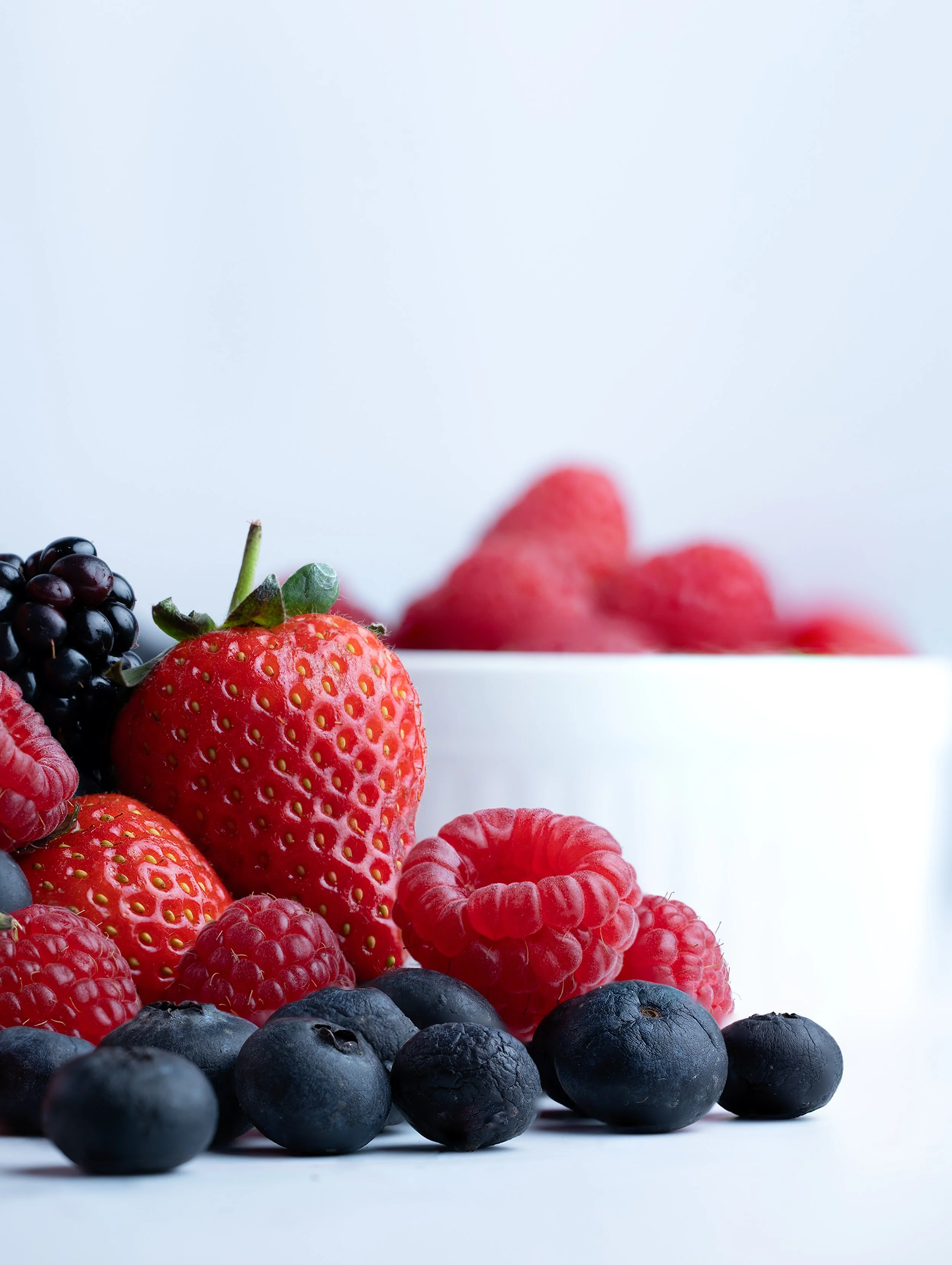 Assorted fresh berries including strawberries, blueberries, raspberries, and blackberries against a light background.