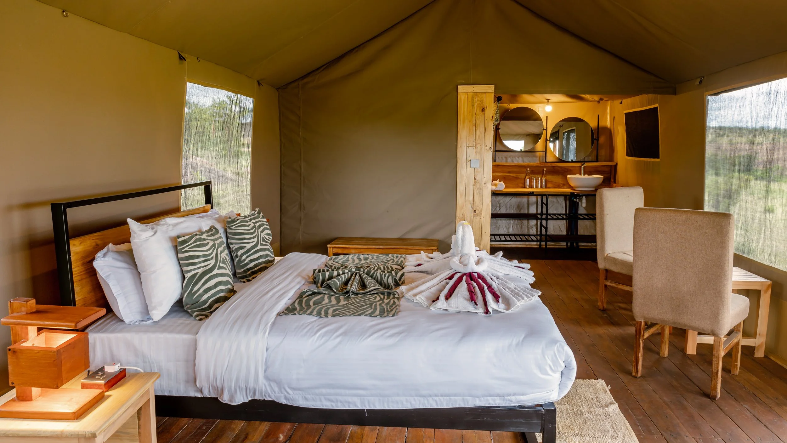 A cozy bedroom with a large bed decorated with zebra-print pillows, wooden furniture, and a small kitchenette area with two circular mirrors and a vessel sink.