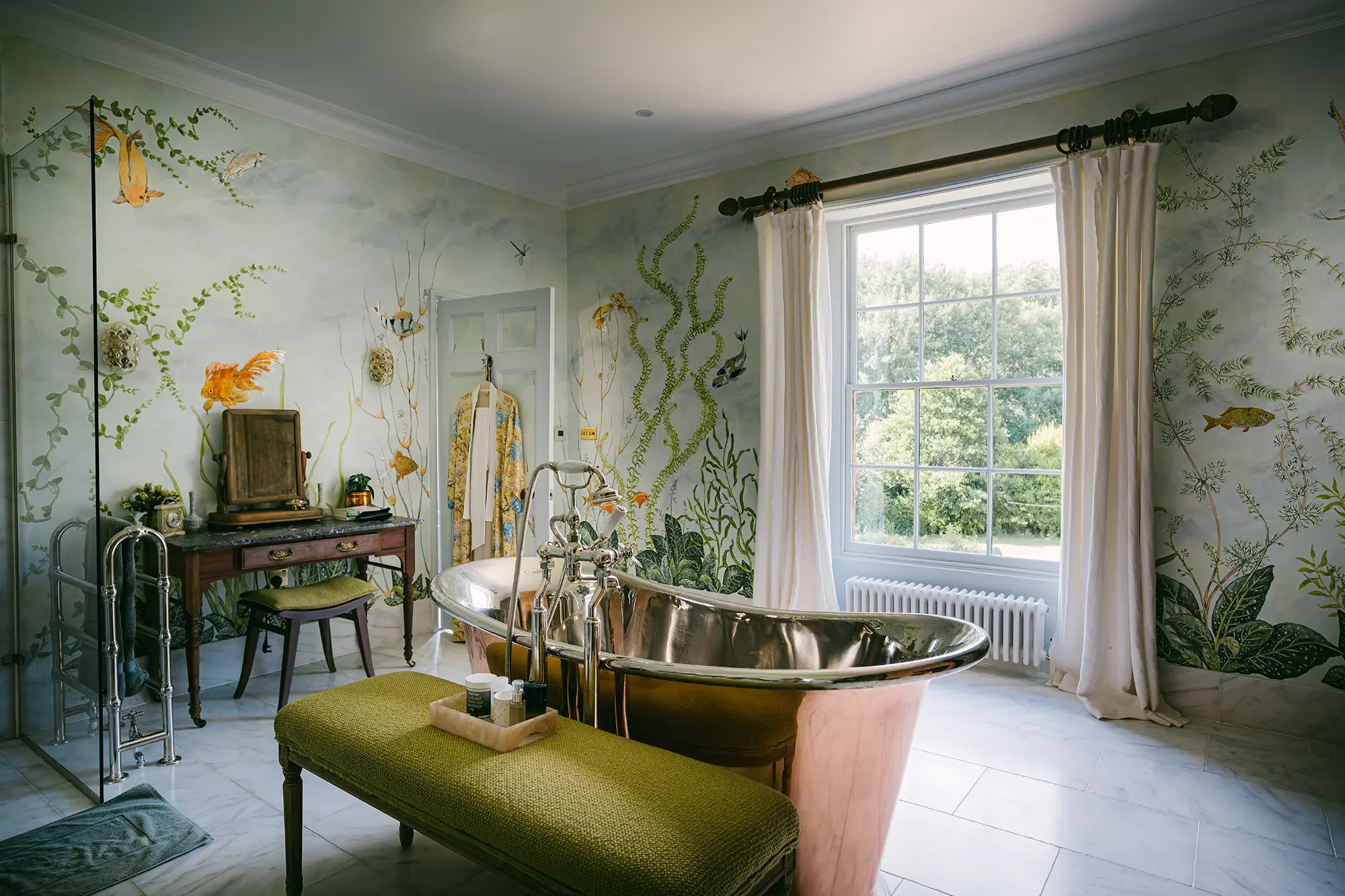 Bathroom with green botanical wall mural, clawfoot bathtub, window with white curtains, and vintage furniture.