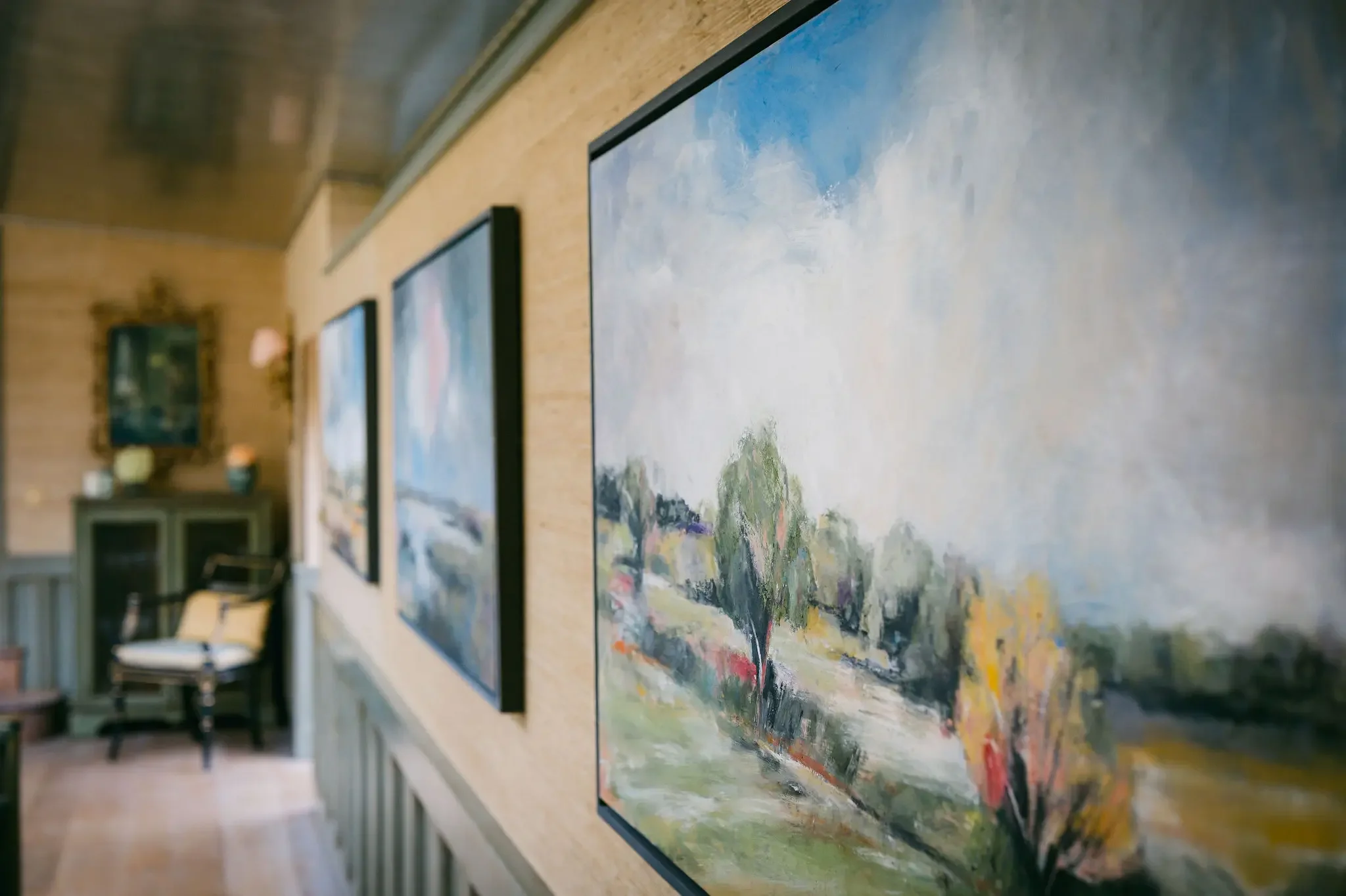Paintings displayed on a wall inside an art gallery, with gallery furniture in the foreground.