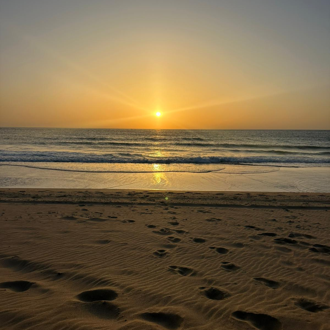 Sunset over the ocean with footprints in the sandy beach in the foreground.