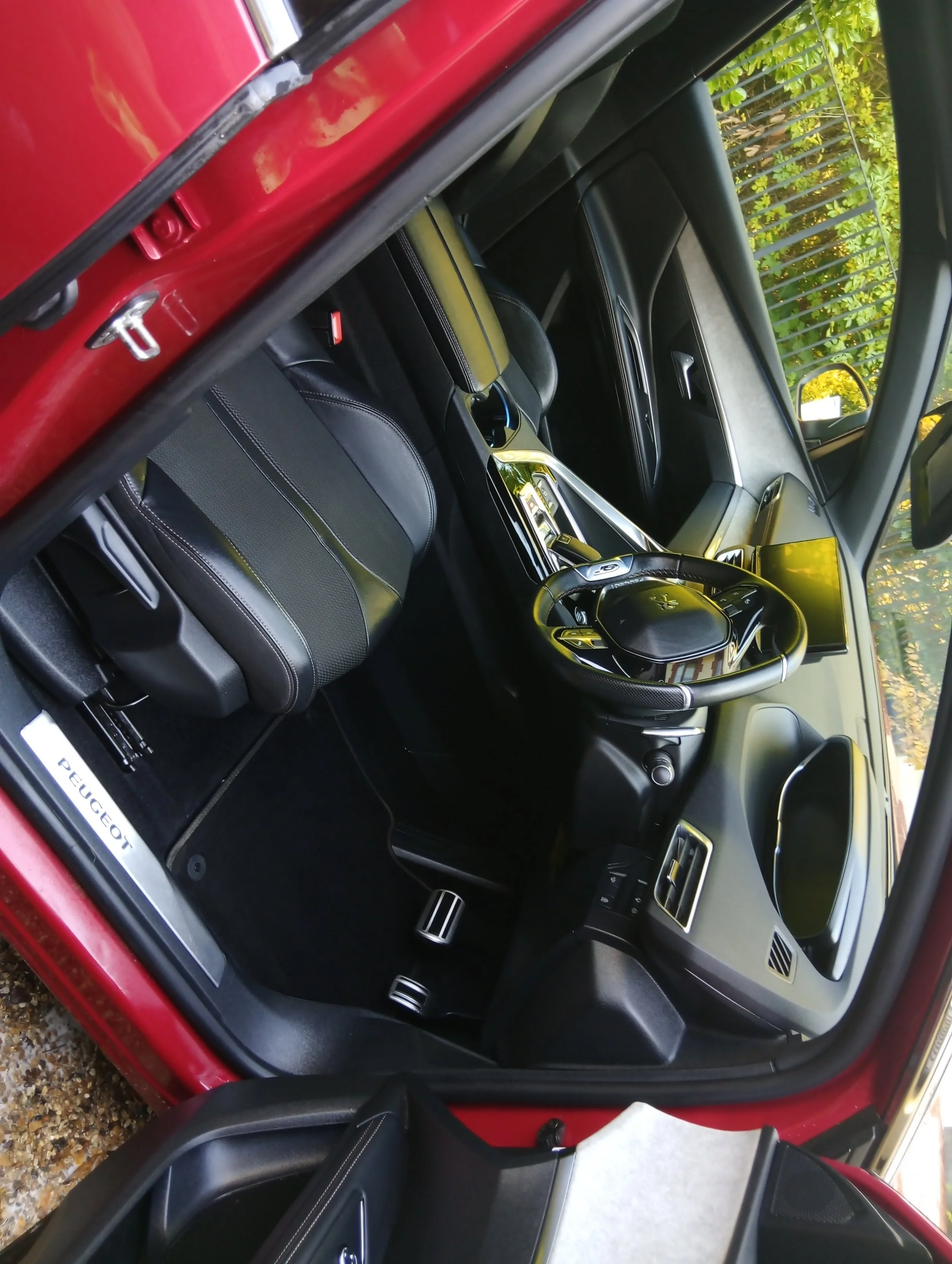 Interior of a red Peugeot vehicle showing the driver's seat, steering wheel, dashboard, and center console.