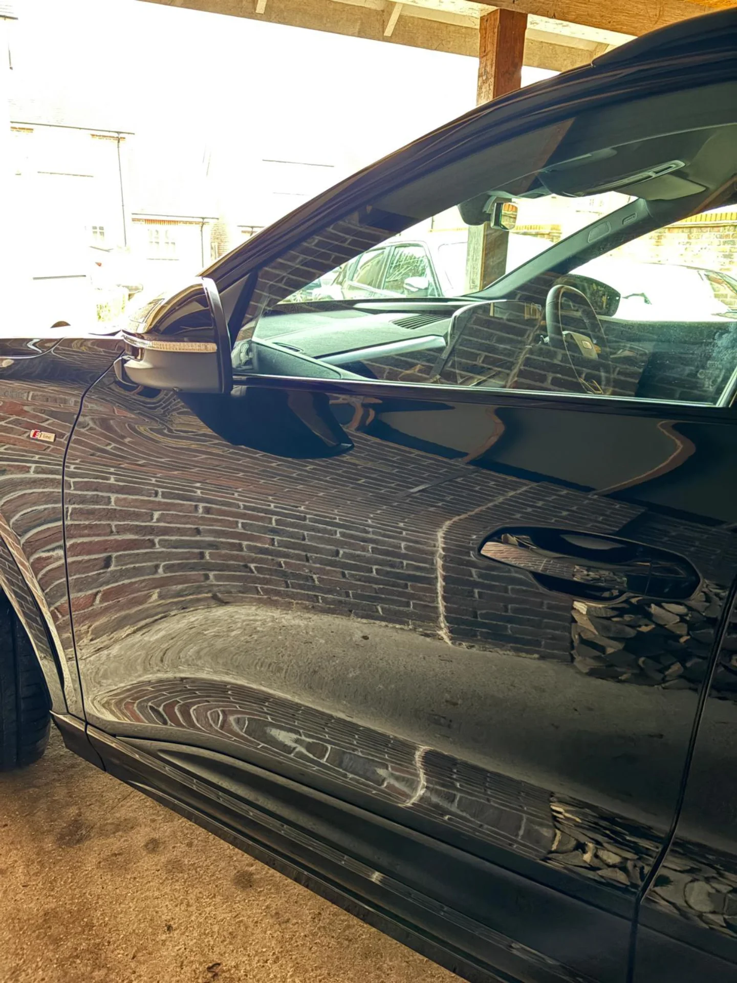 Close-up of a black car with a reflection of the brick wall and garage interior on its side.
