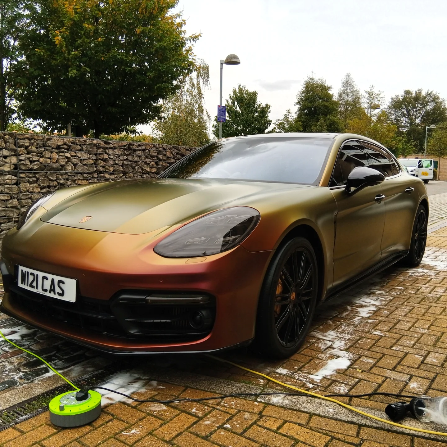 A luxury Porsche car with a bronze and black color gradient parked outdoors on a wet brick surface.