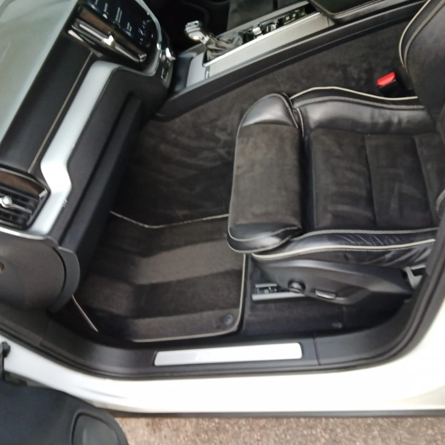The interior of a luxury car showing the driver's seat and part of the dashboard with a modern gear shift. The seat has black leather and fabric upholstery with contrast piping.