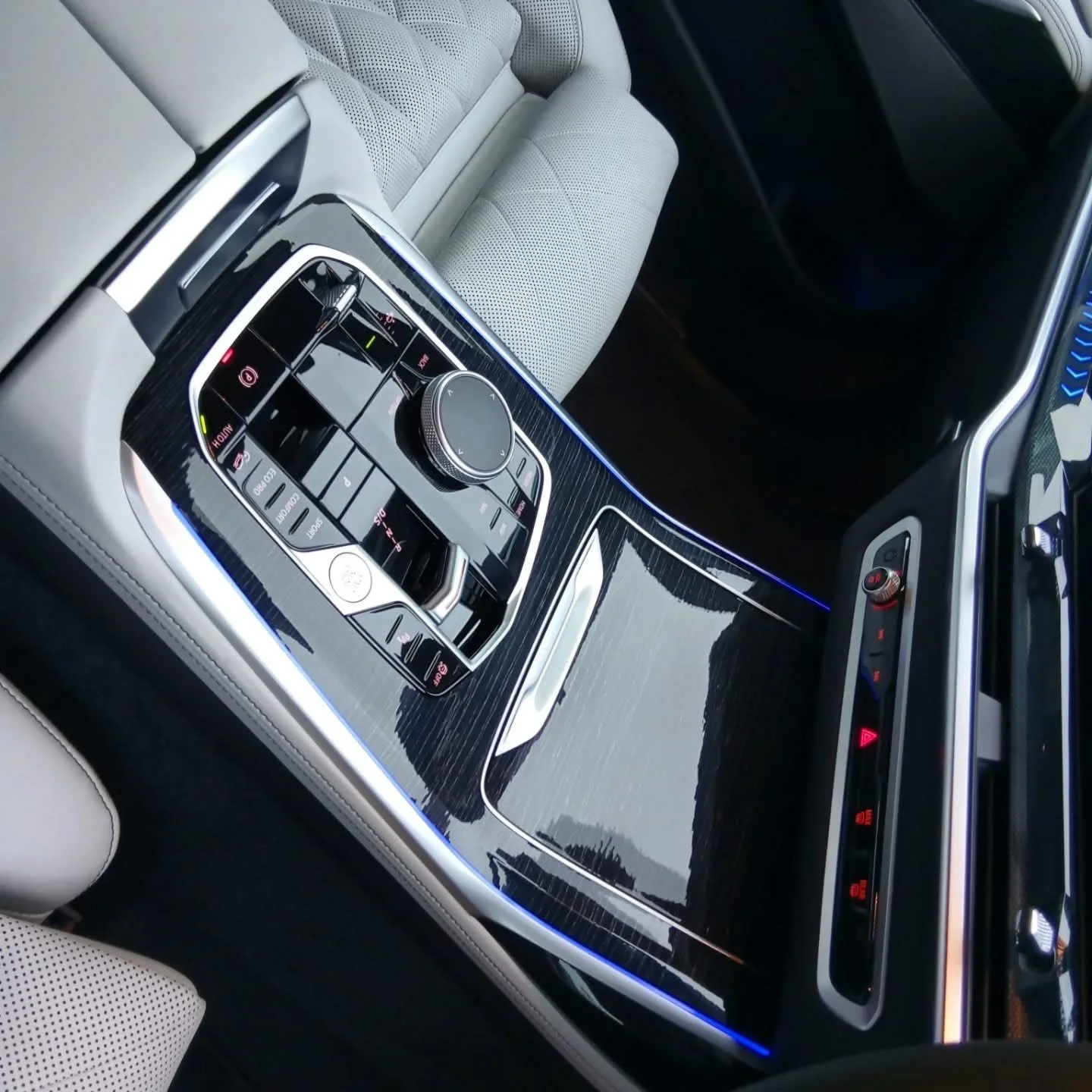 Interior of a luxury car showing a sleek, modern center console with control buttons, a rotary knob, and a strip of ambient blue lighting.