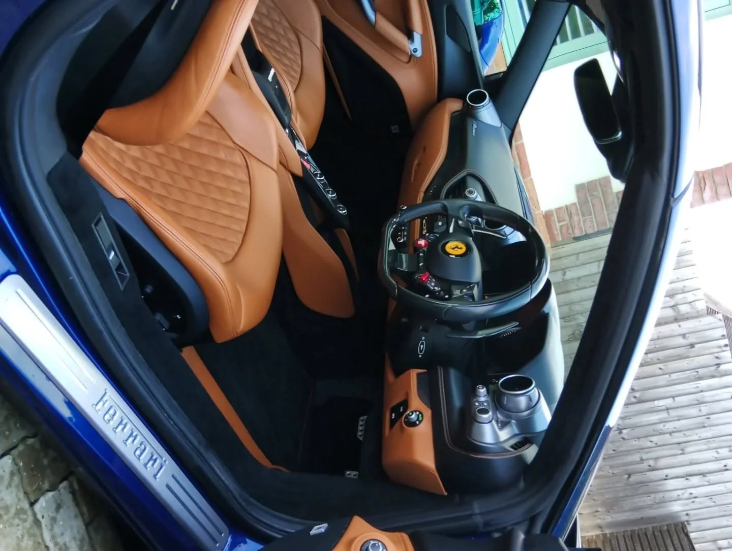 Interior of a luxury blue Ferrari sports car with tan leather seats and modern dashboard controls.