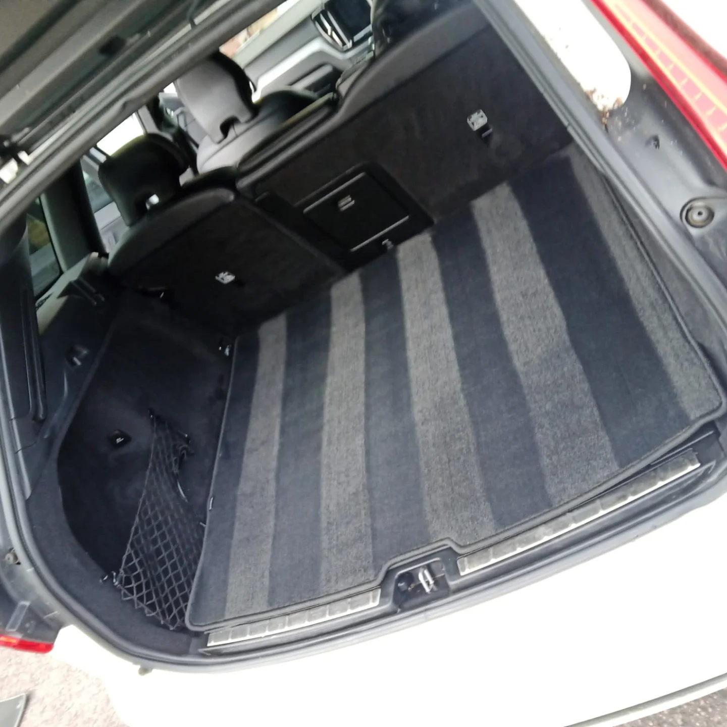 Empty car trunk with dark carpeted interior and side netting, showing the back of the rear seats and part of the rear bumper.