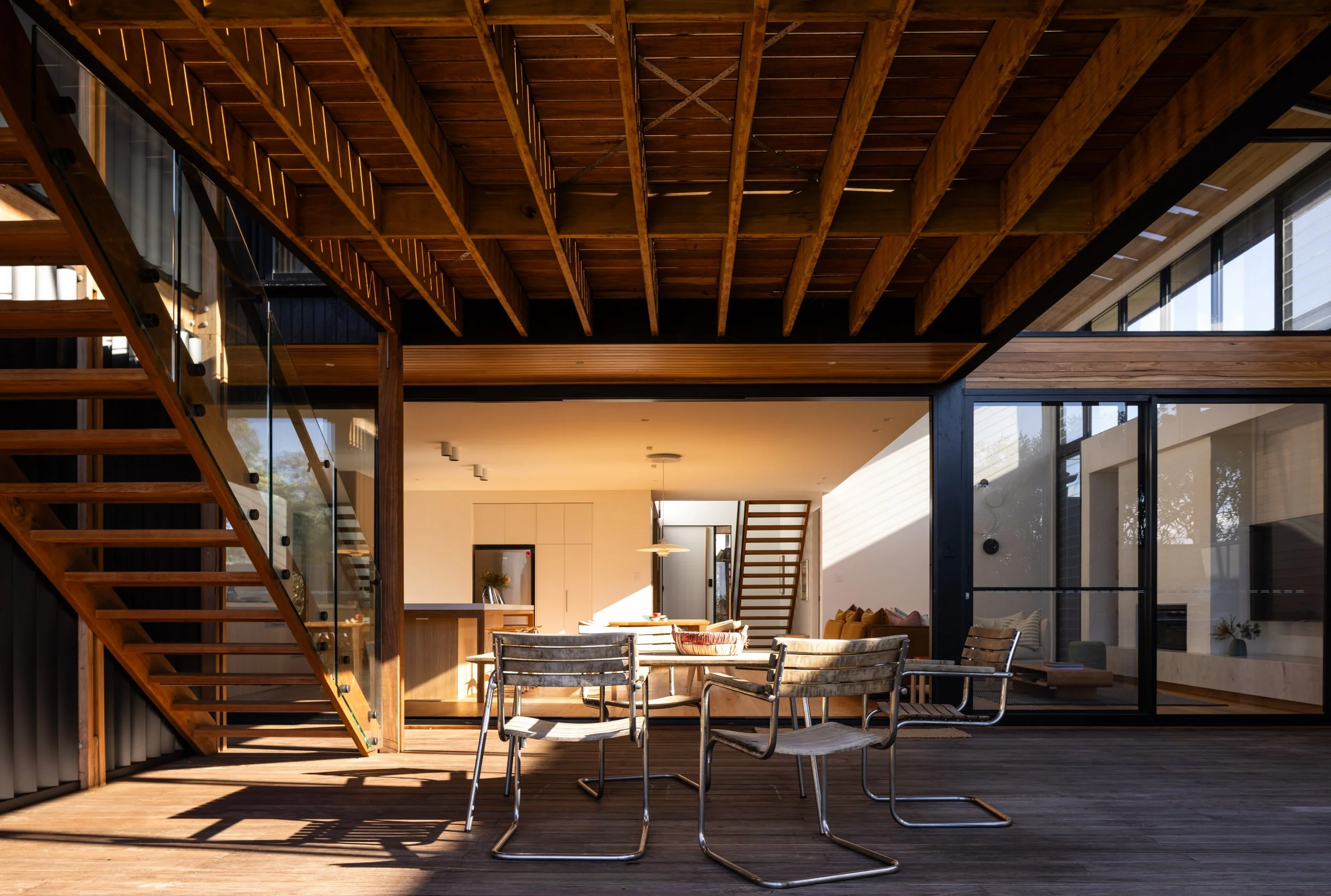 Modern open-concept living space with wooden balcony, staircase, and outdoor dining area
