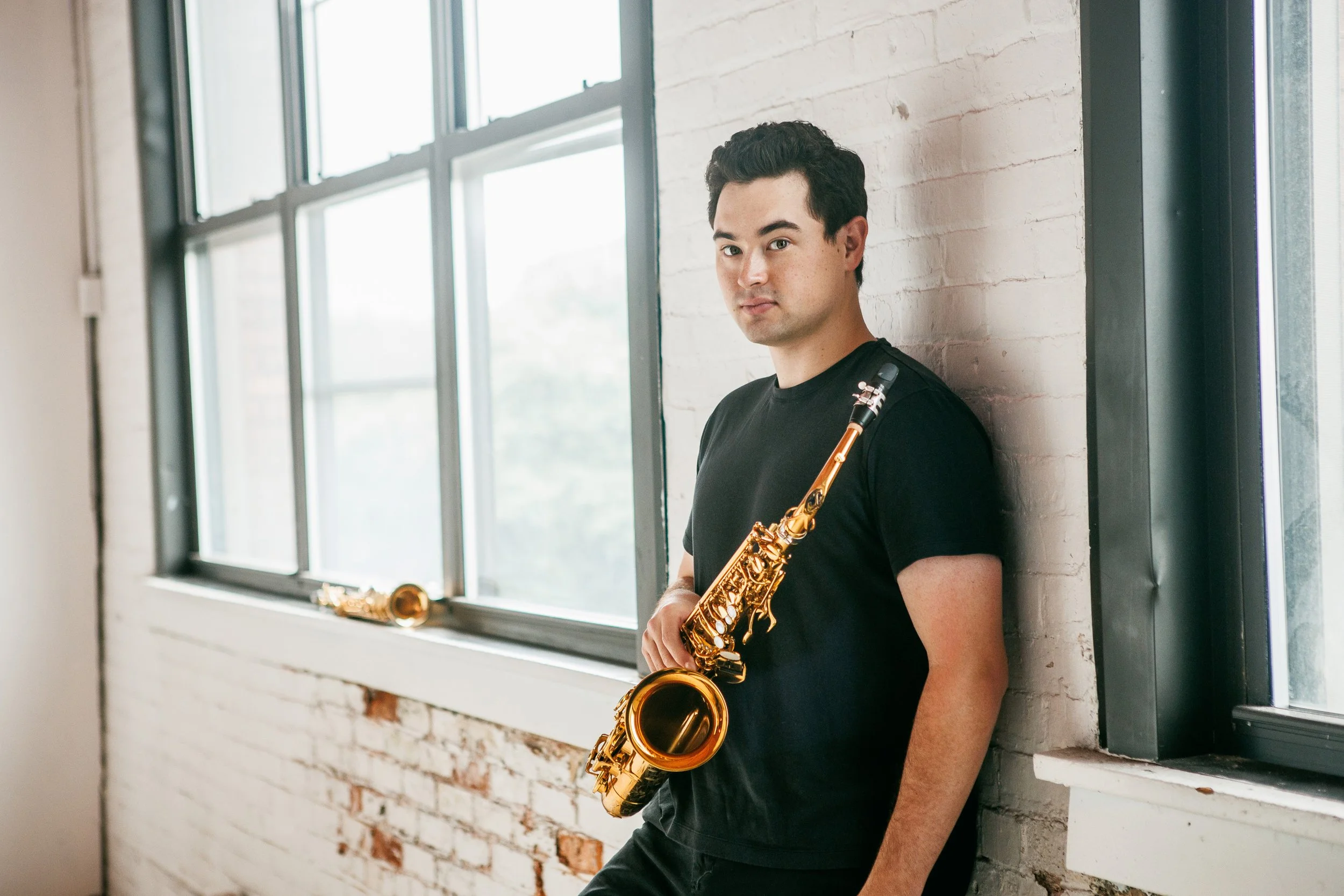 Landon Chang, University at Buffalo saxophone professor, holding an alto saxophone in a modern music studio setting