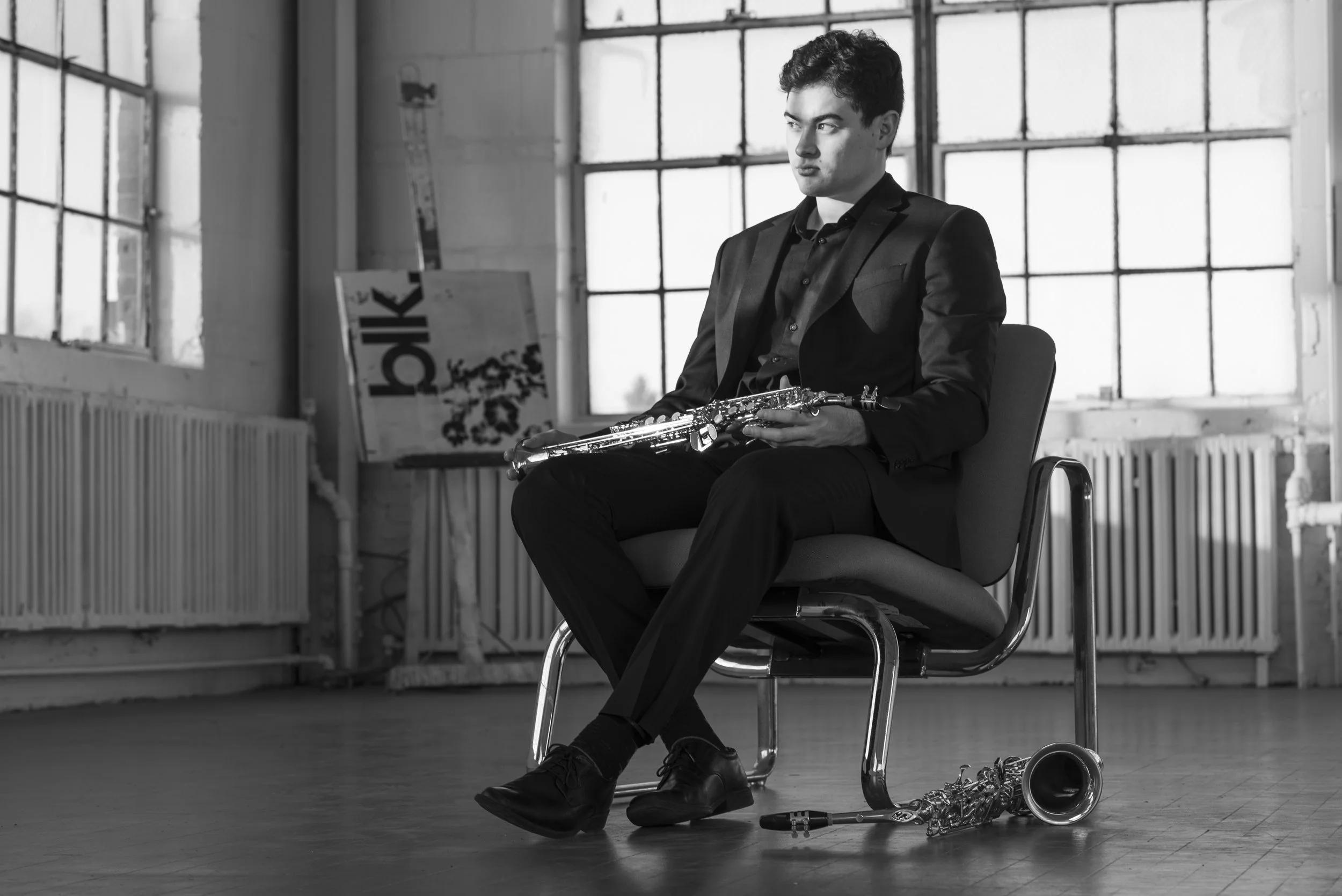 Black and white portrait of Landon Chang, contemporary saxophonist and educator, in an industrial Rochester studio with alto and soprano saxophones