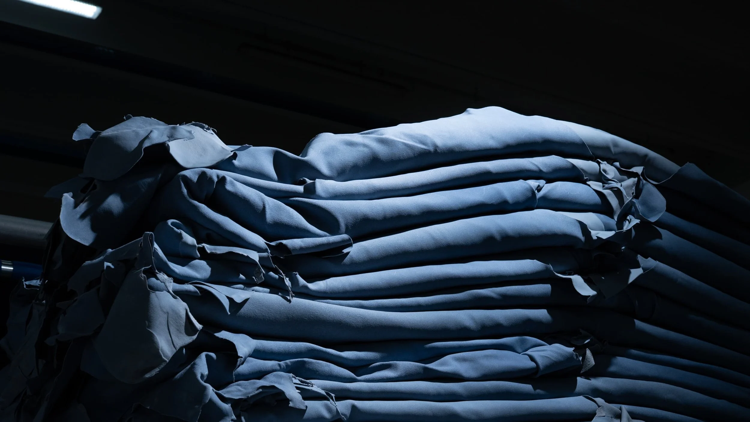 Pile di tessuti o vestiti ammucchiati, con luce e ombre che creano un effetto drammatico.