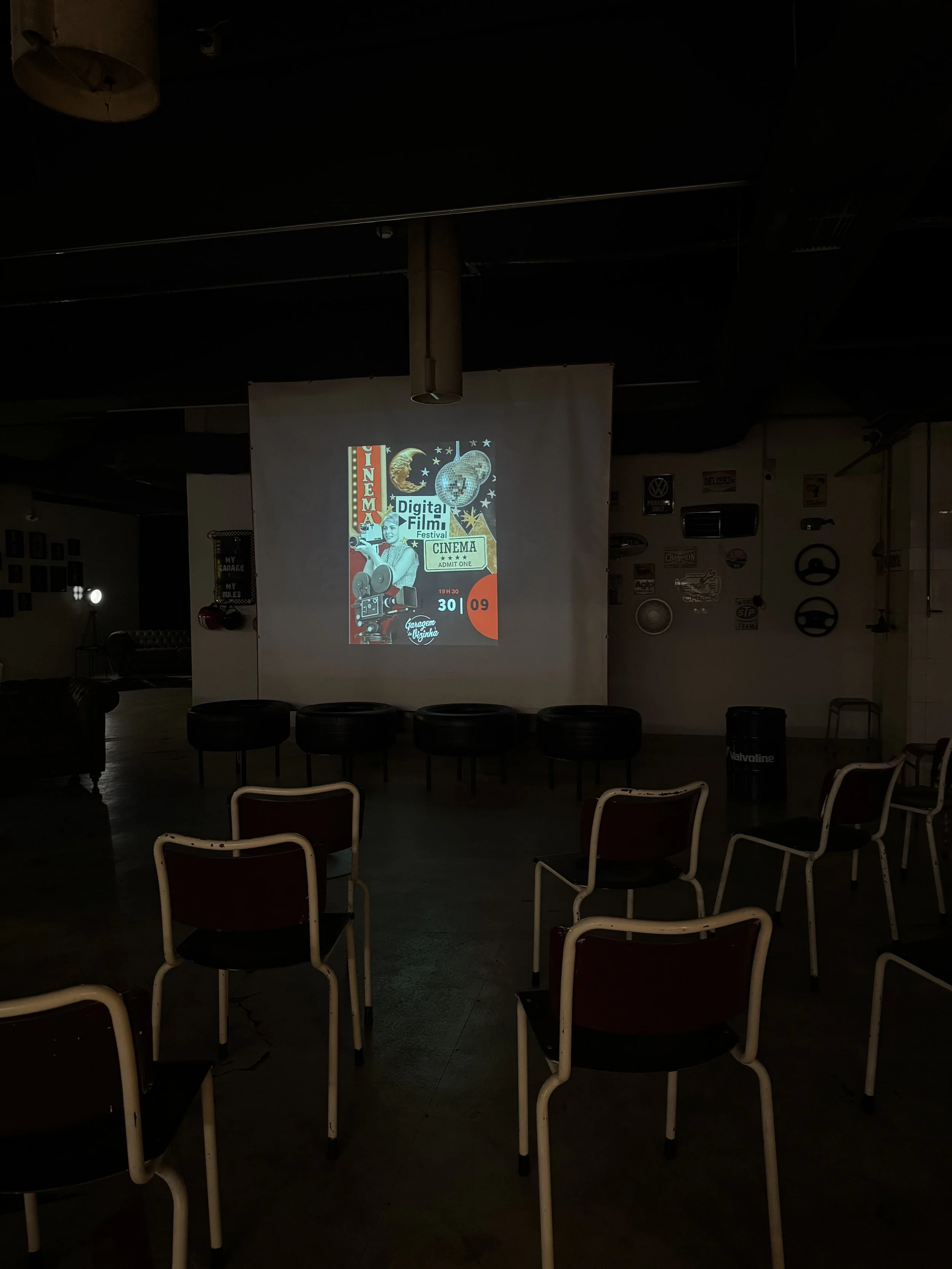 Sala de cinema com cadeiras e tela projetando pôster de festival de filmes digitais.